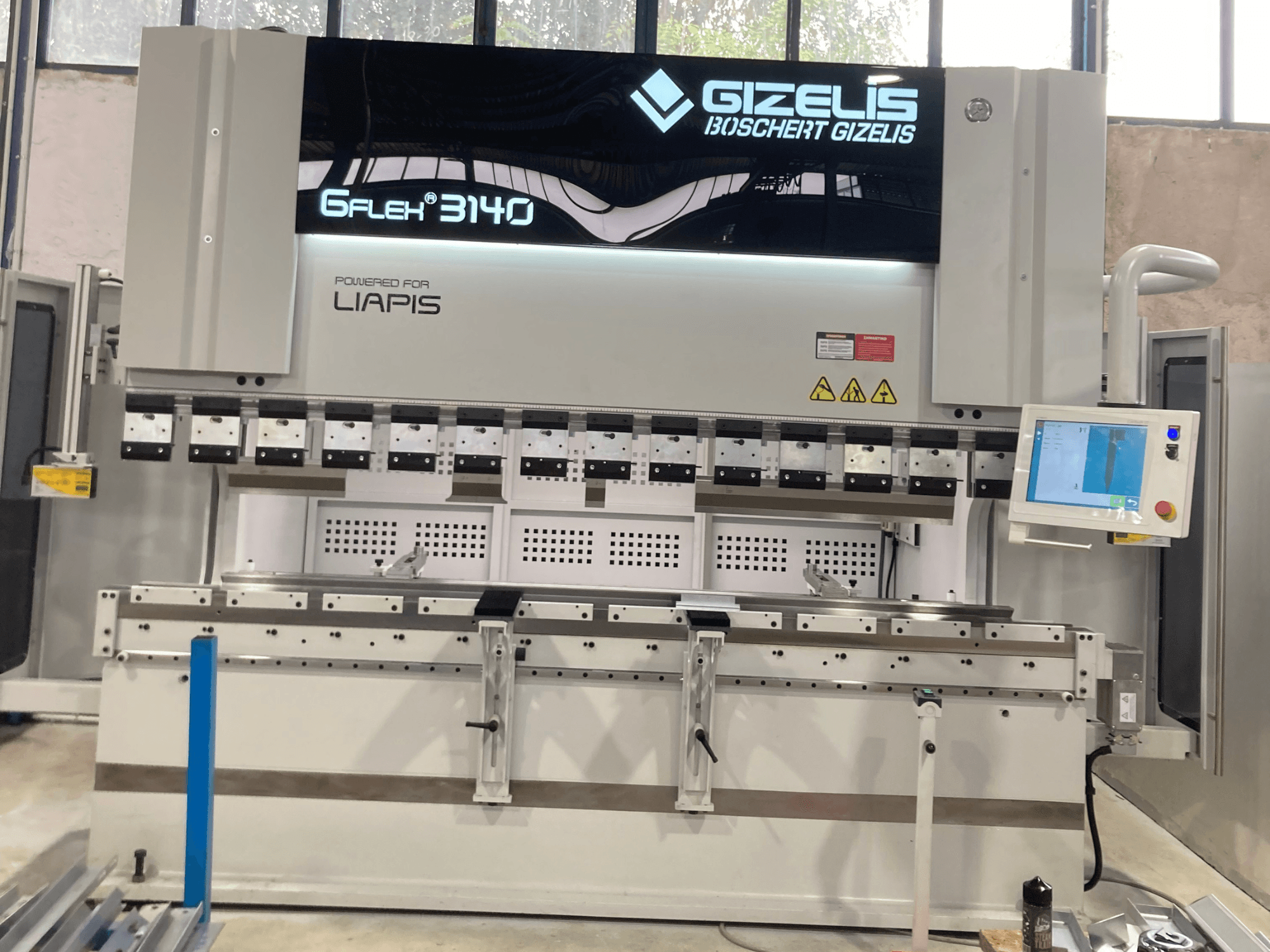 Hüdrauliline press GIZELIS G-FLEX 3140 esiplaanil koos juhtimisekraaniga, millel on mitu painutusvahendit ja ohutussildid.