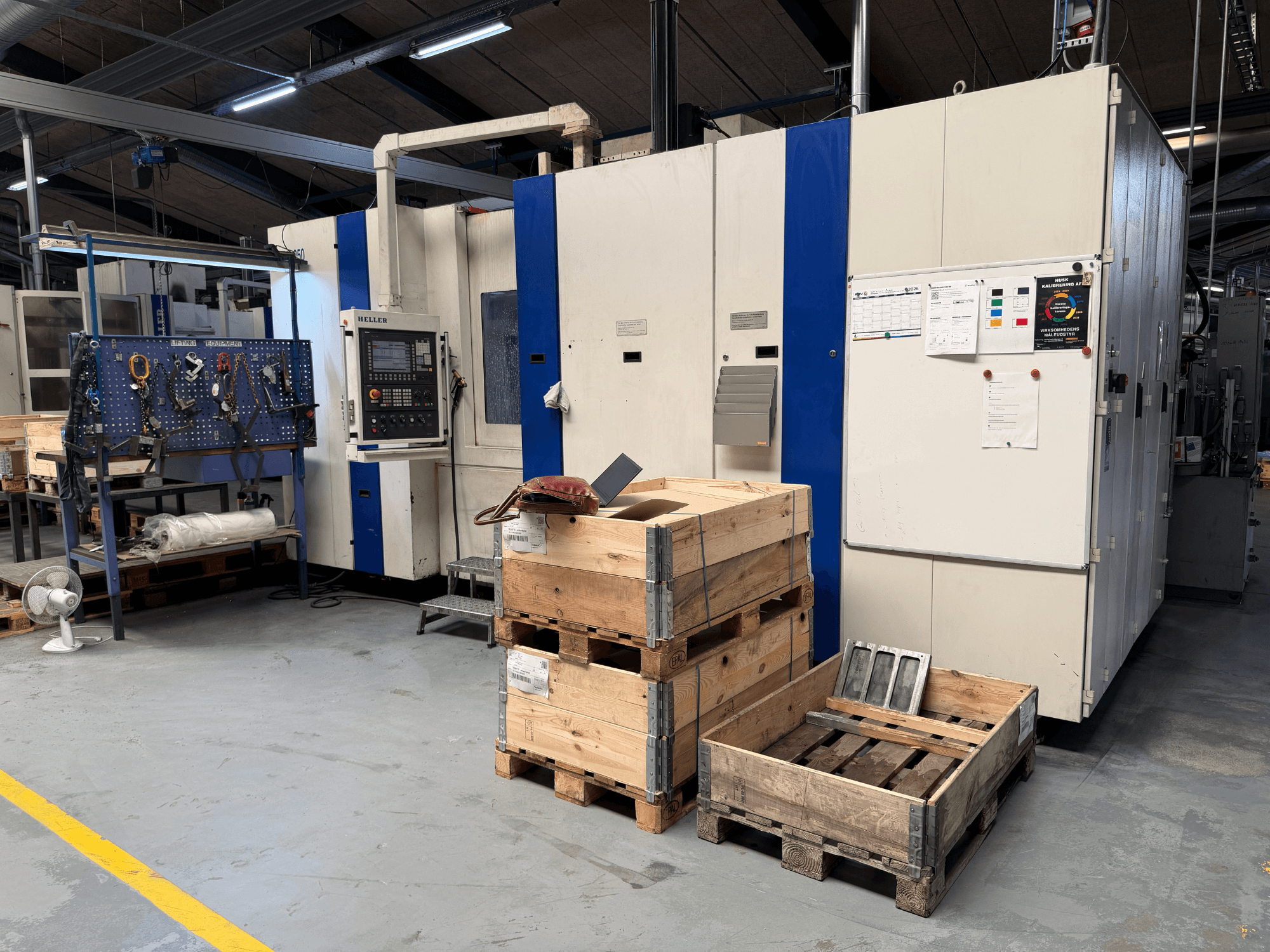 HORIZONTAL MACHINING CENTRE HELLER MCH 250 töökojas, külgvaade, kus on näha puidust kaubaalused ja tööriistahoidik.