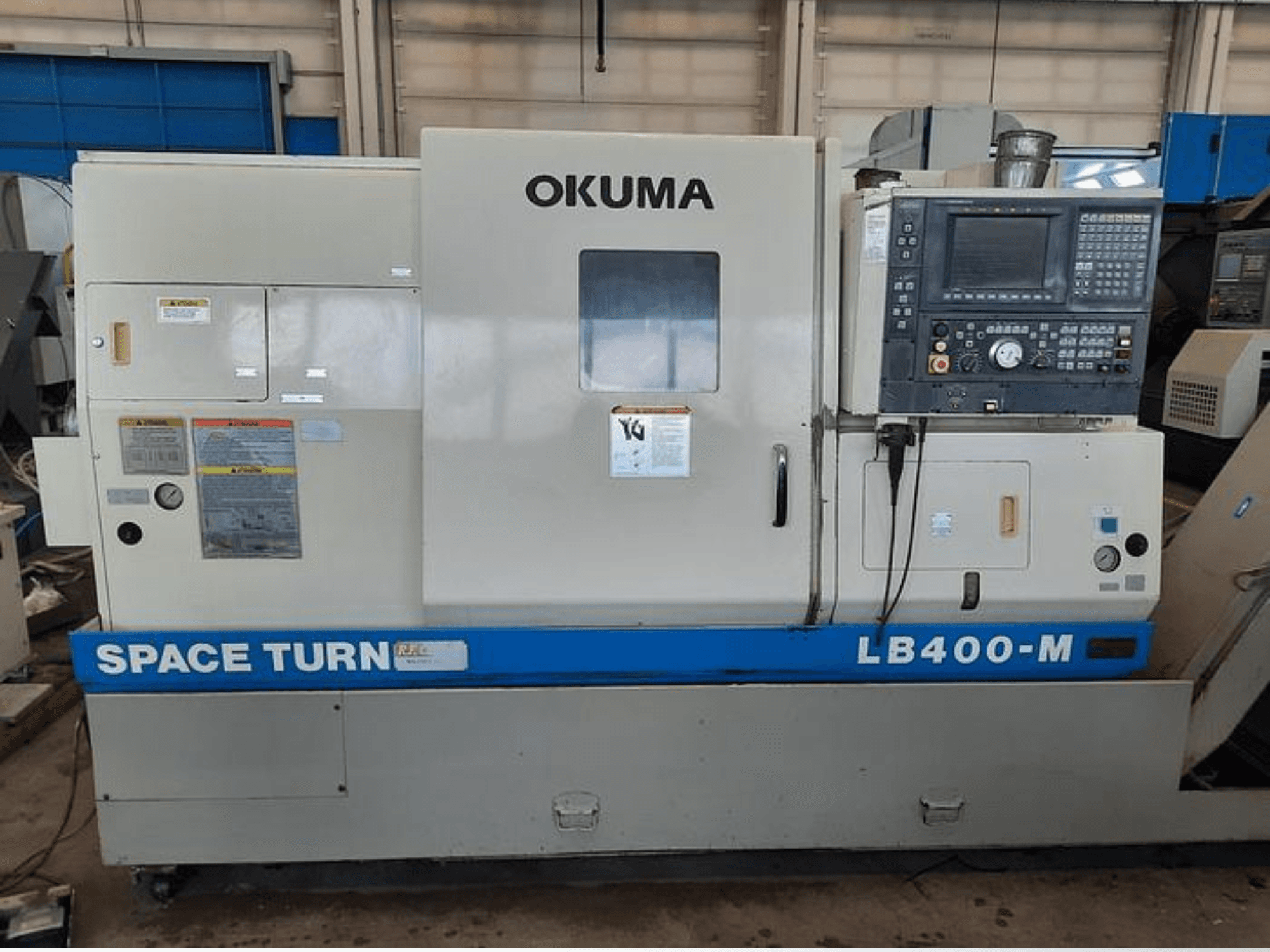 Okuma LB400-M CNC-tööpink, esikülg, juhtpaneel, hoiatussildid ja sinine "SPACE TURN" märgistus.