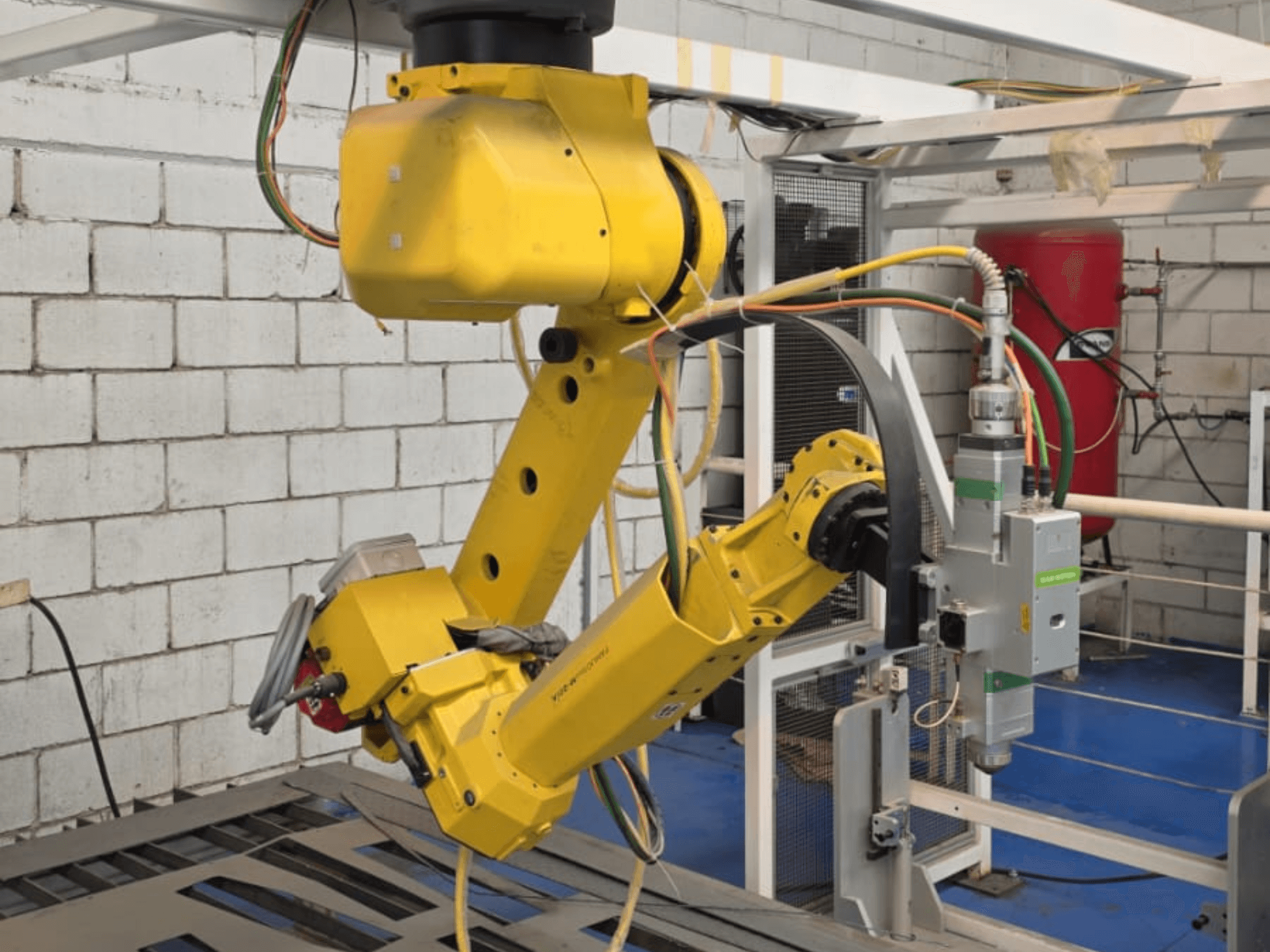 Kollane robotkäsi koos täppistööriistaga, millel on mitu liigendit ja kaablit, vaadatuna tööstuslikus keskkonnas esiplaanilt.