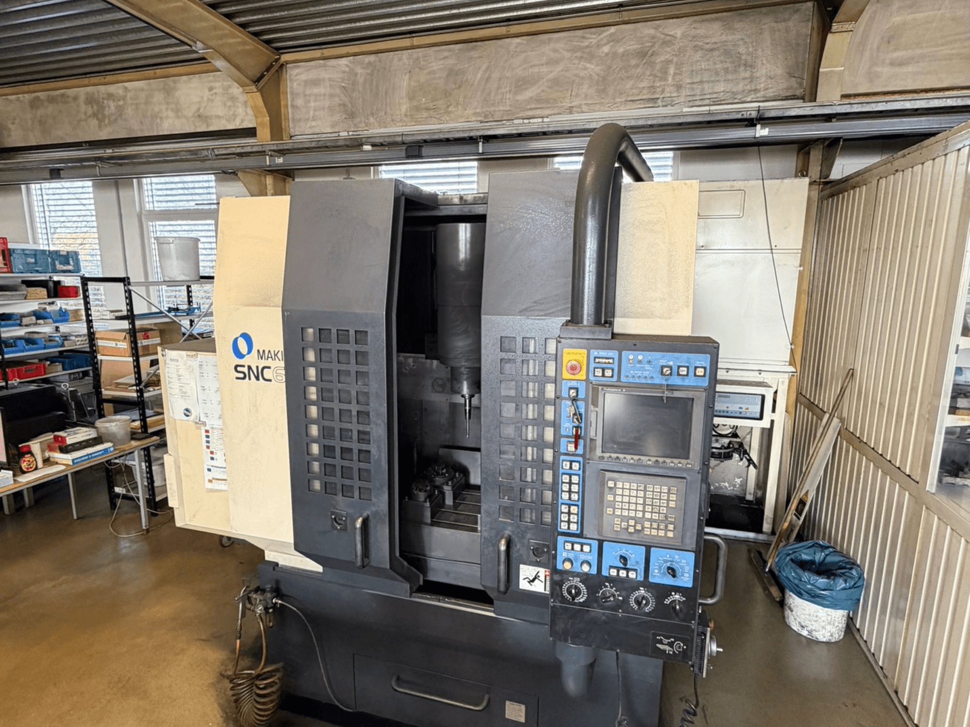 Makino SNC 64-A15 vertikaalne töötlemiskeskus esiplaanil, kus on näha juhtpaneel, töötlemisala ja tööstuslik tööruum.