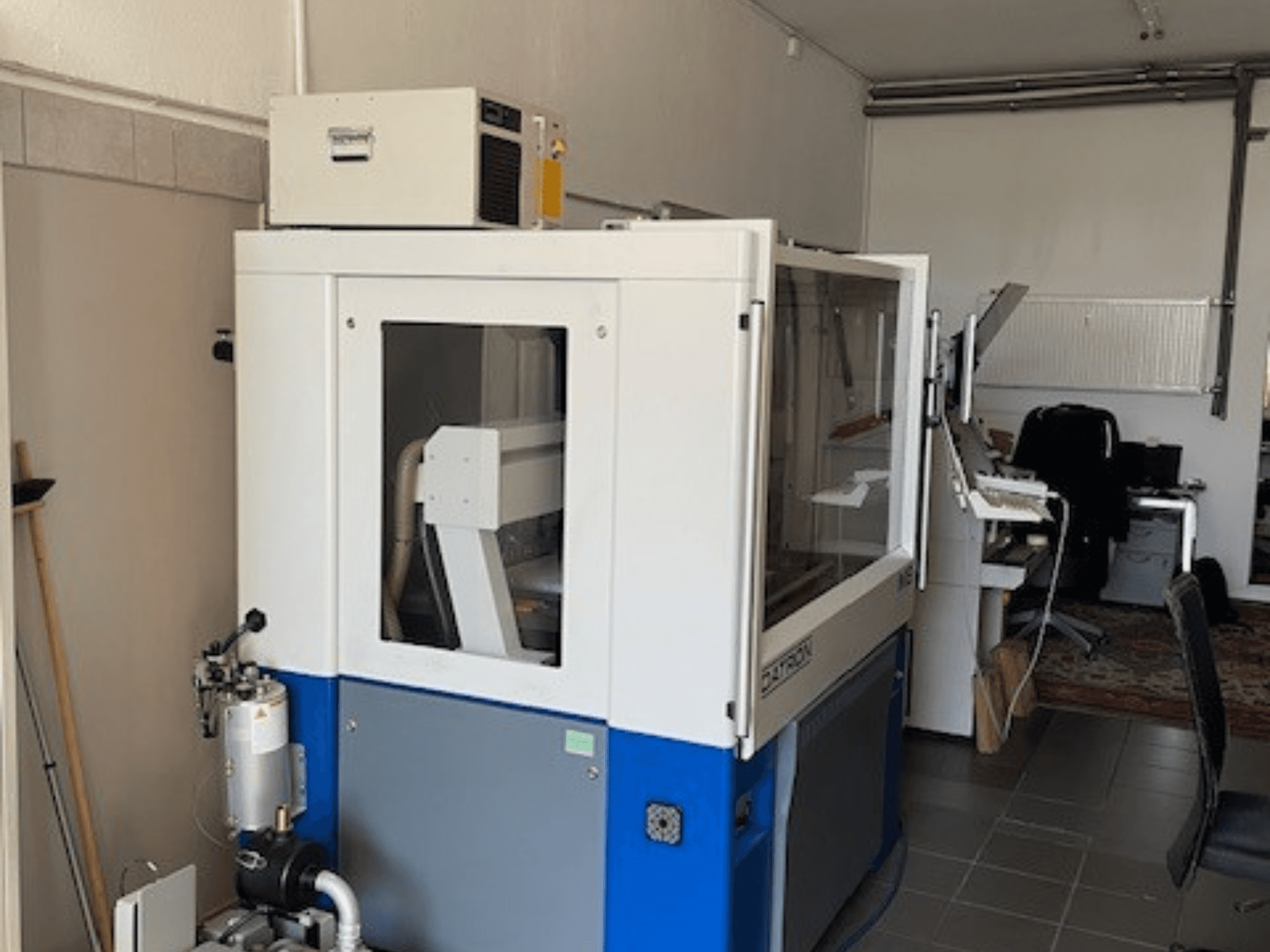 Sinine ja valge tööstuslik masin läbipaistvate paneelidega, esiplaanil, sisaldab juurdepääsu juhtimissüsteemile ja nähtavat ventilatsiooniüksust.