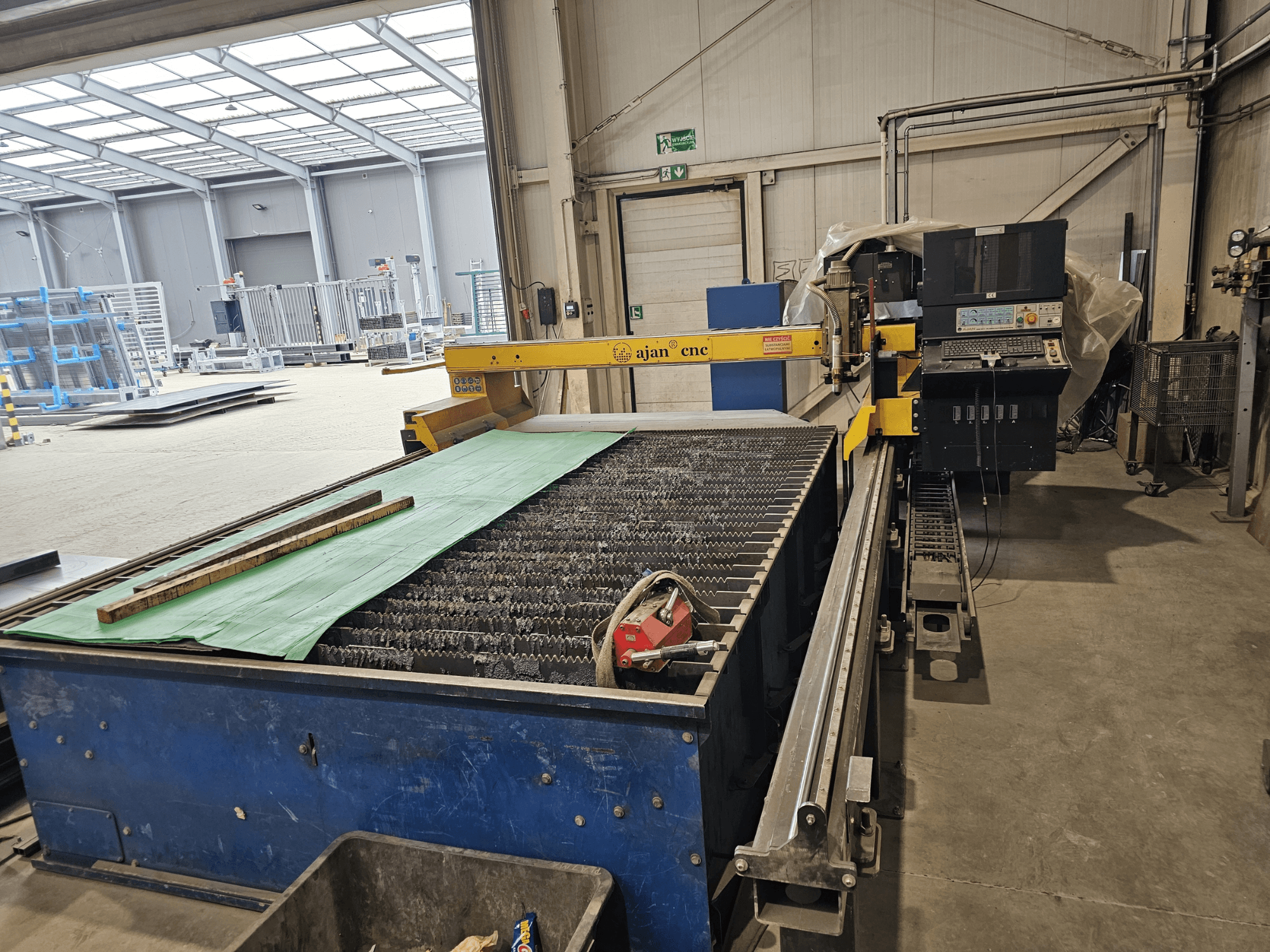 AJAN PP16011 Automaatne plasmalõikepink külgvaates, millel on lõikelaua ja juhtpaneel, seadistatud töökojakeskkonda.