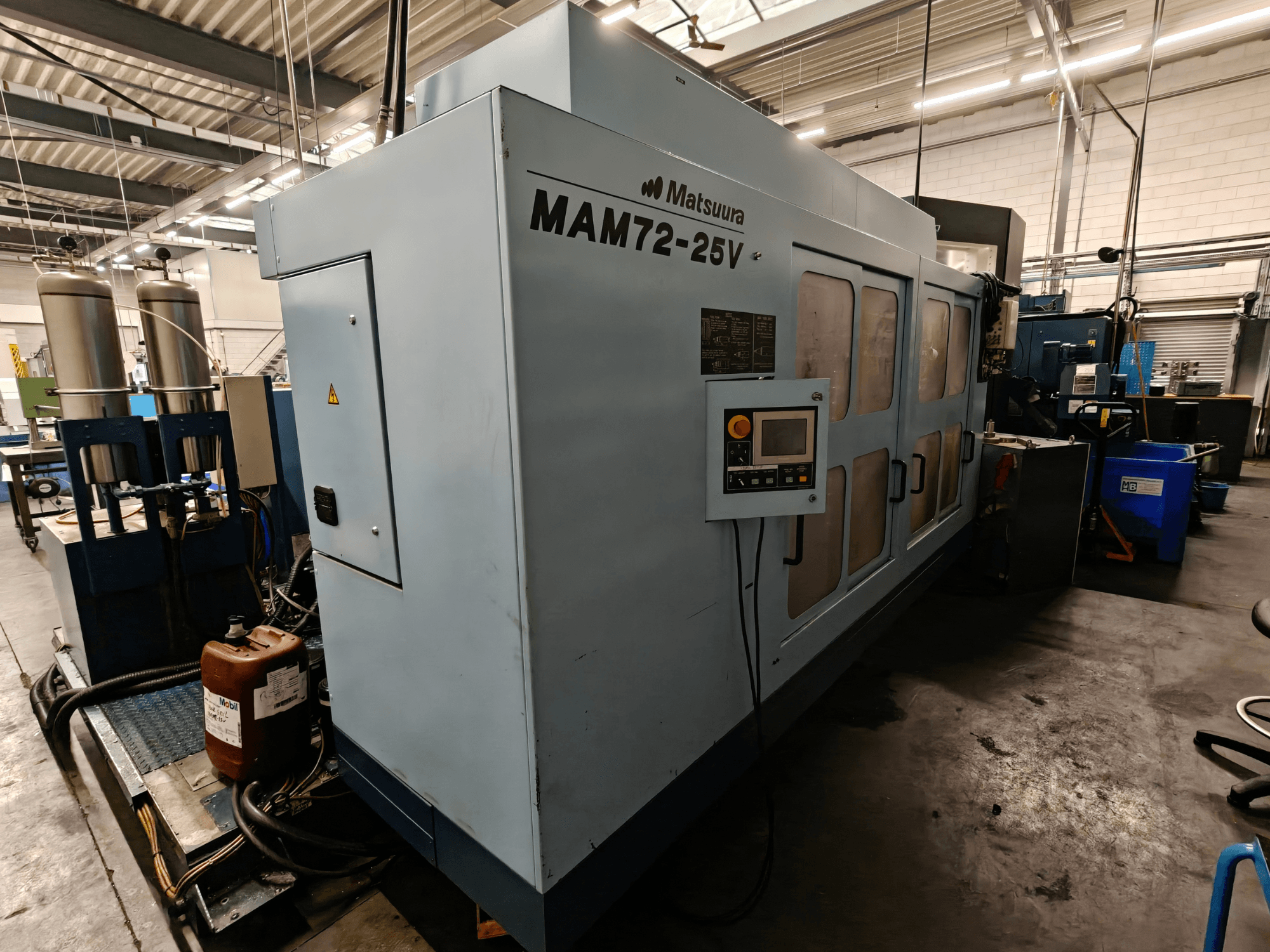 Matsuura MAM72-25V CNC-pink, külgvaade, juhtpaneel, kaks jahutusvedeliku paaki ja tööruum tööstuslikus keskkonnas.