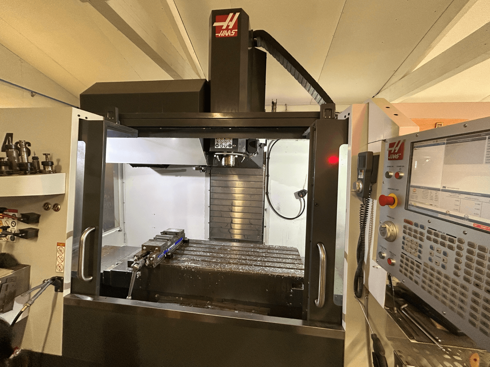 HAAS VF-4SS vertikaalne töötluskeskus, esiplaan, kus on näidatud juhtpaneel, tööriistahoidja ja tööpiirkond koos metallilaastudega.