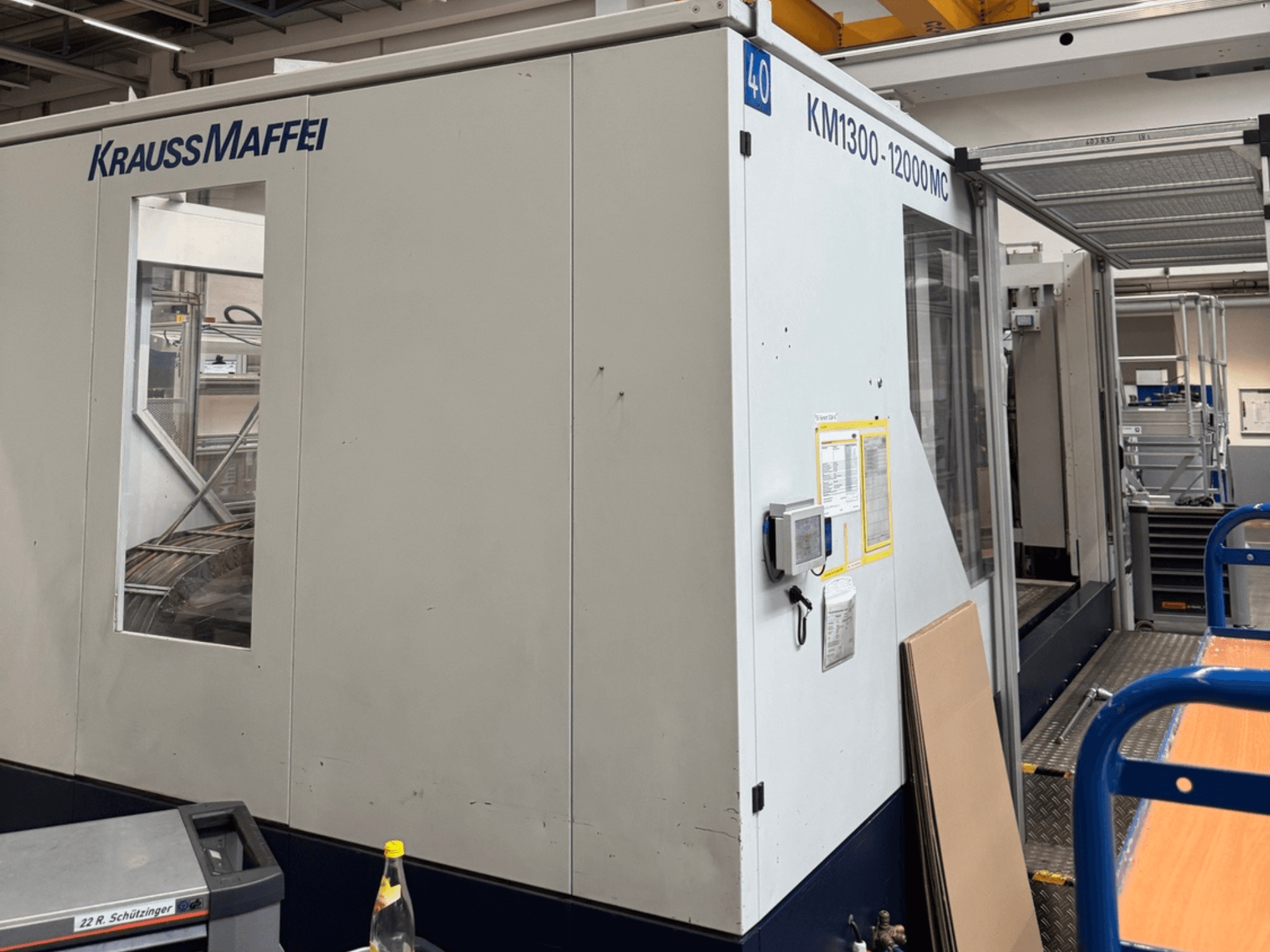 Krauss Maffei hüdrauliline survevalu masin KM1300-12000 MC, külgvaade, kus näidatakse juhtpaneeli ja tööruumi.