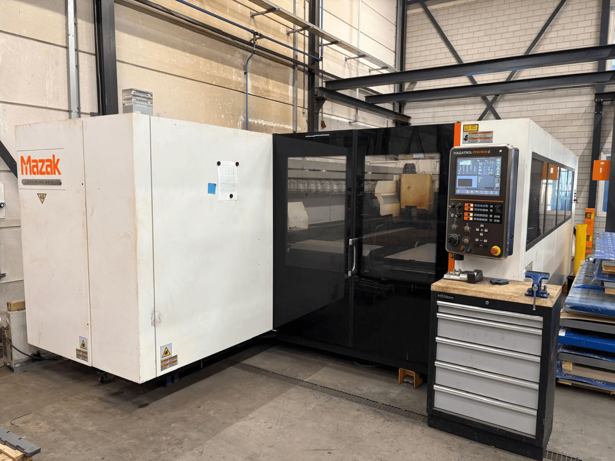 Mazak Optiplex 3015 CO₂-laserlõikepink, vaade eest, millel on näha juhtpaneel ja tööstuslik paigutus.
