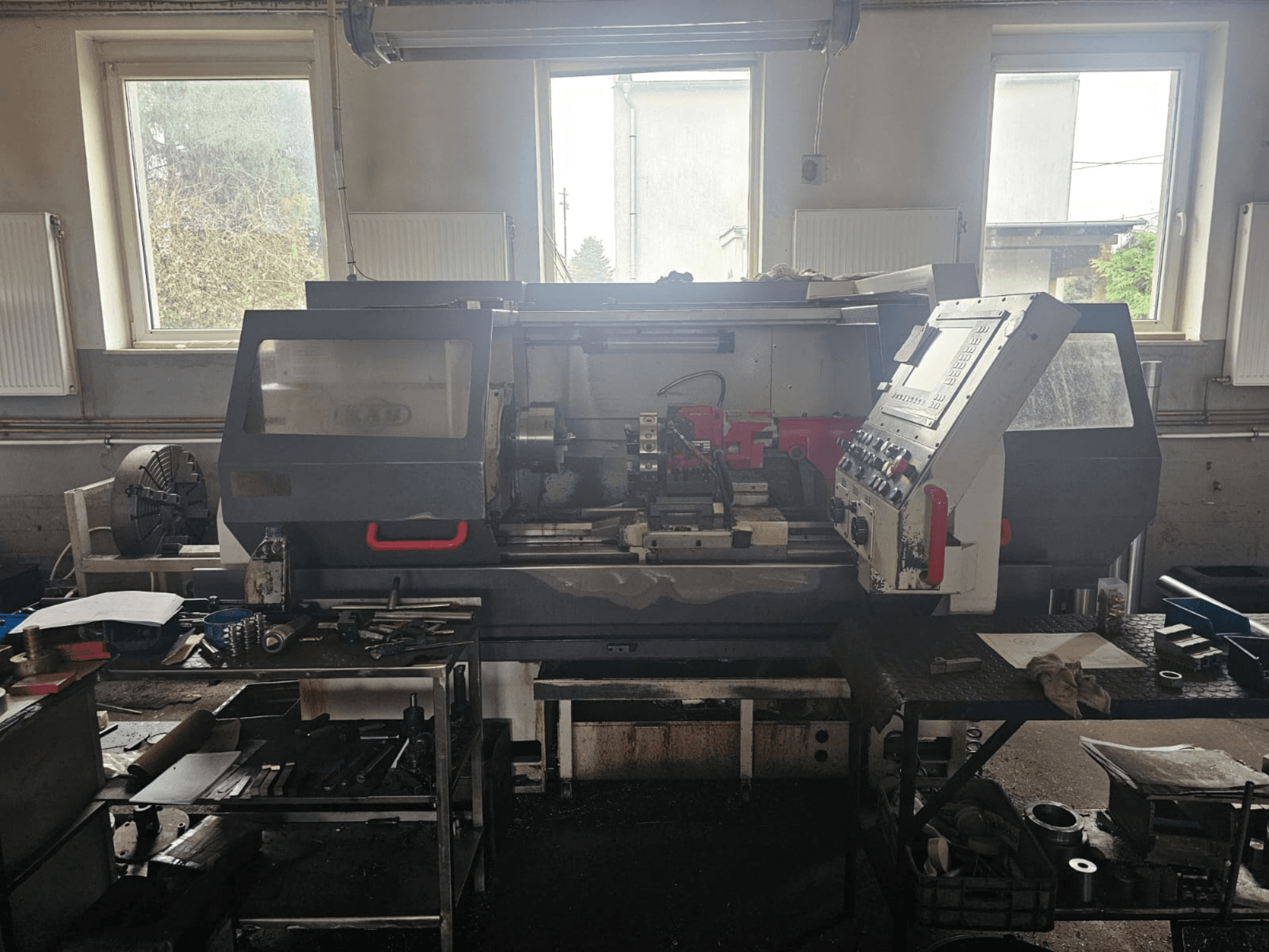 Treipingi töökojas, esiplaanil, juhtpaneel ja tööriistad laudadel, ümbritsetud akendest ja korrastatud tööruumist.