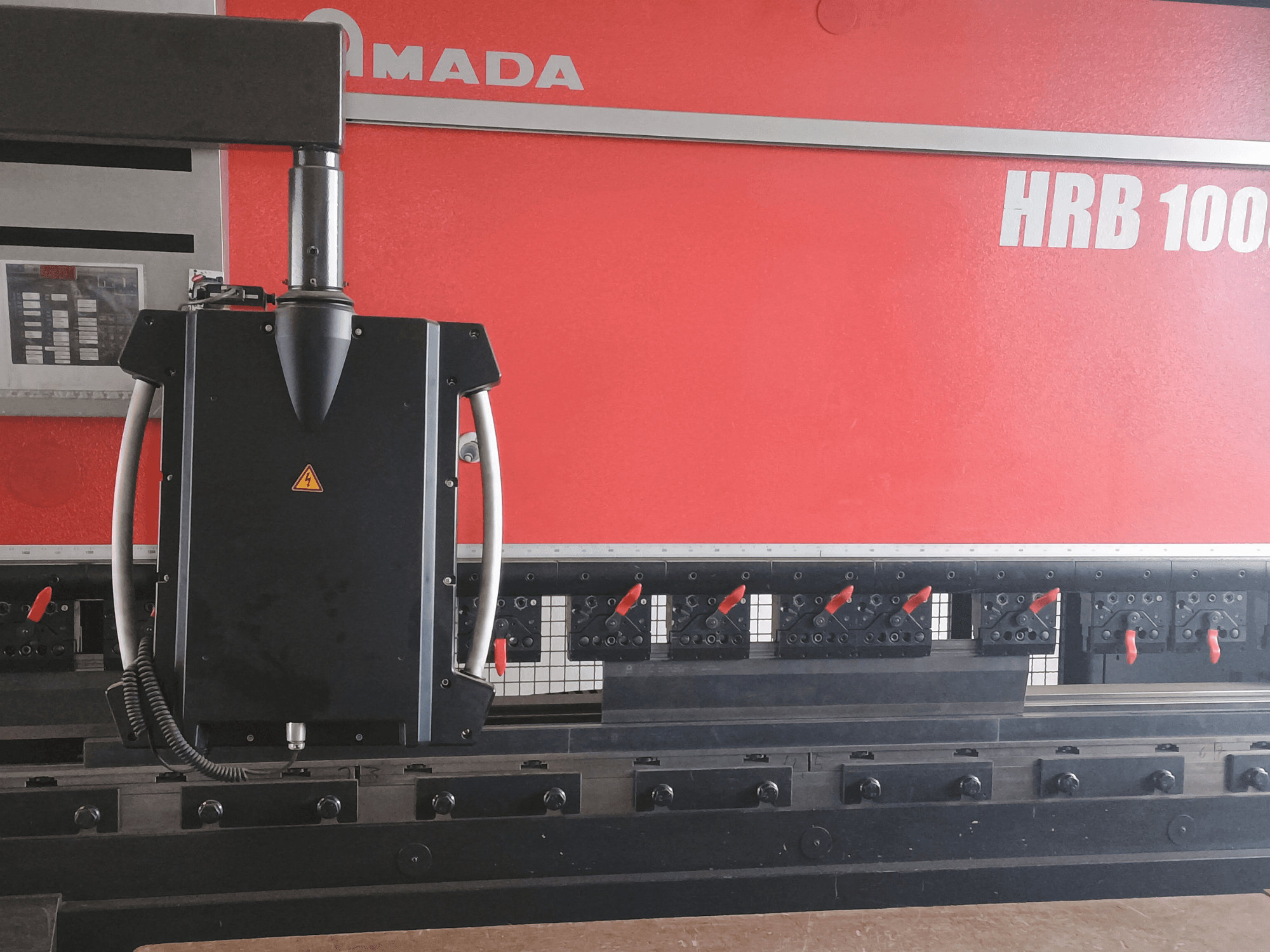 Amada HRB 100 painutuspingi esivaade; must juhtpea koonilise pihusti ja reguleeritavate klambritega.