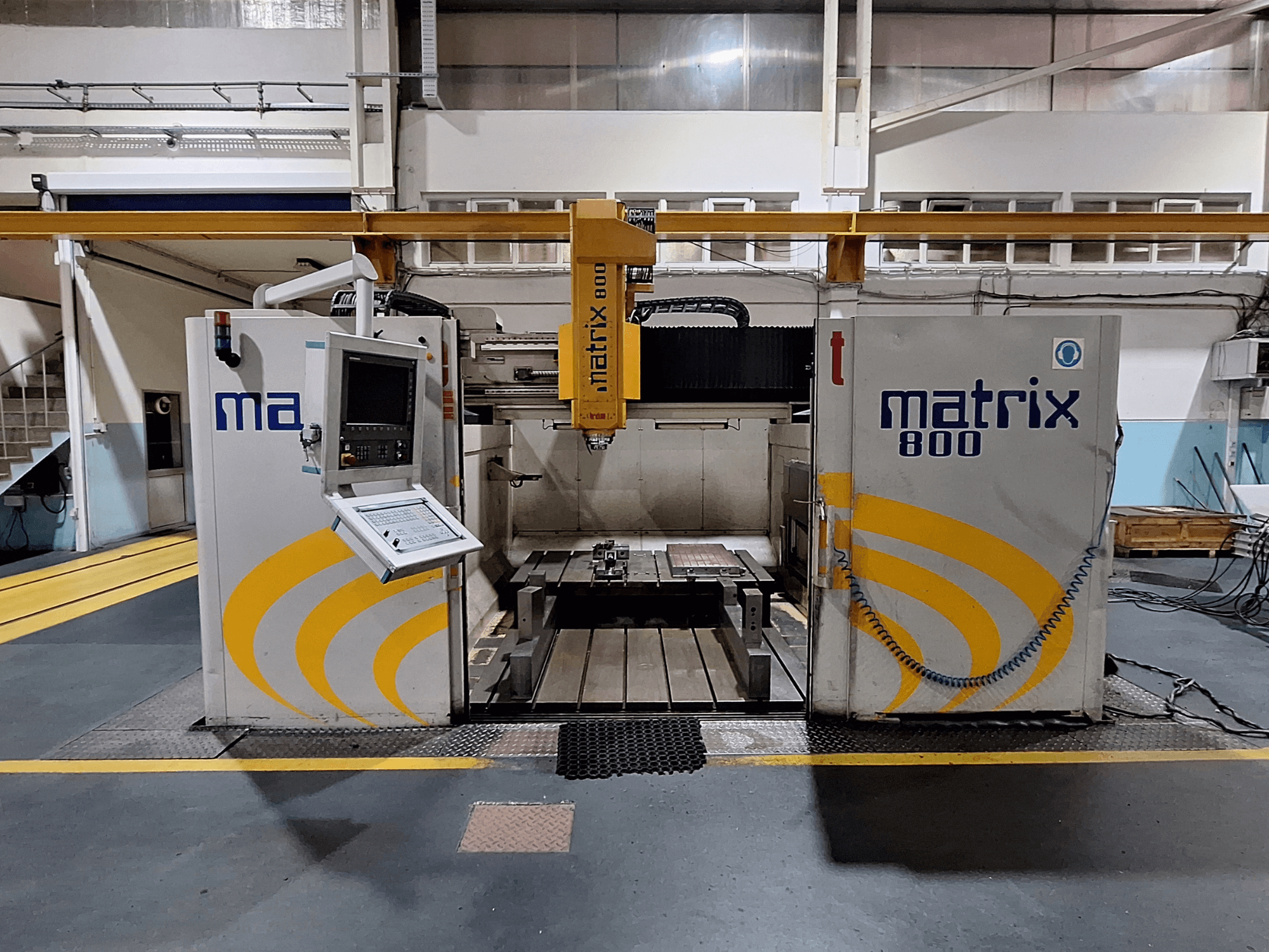 Gantry-freesping Breton Matrix WM 800 K25 töökojas, kus on näidatud juhtpaneel ja töölaud esiplaanilt.