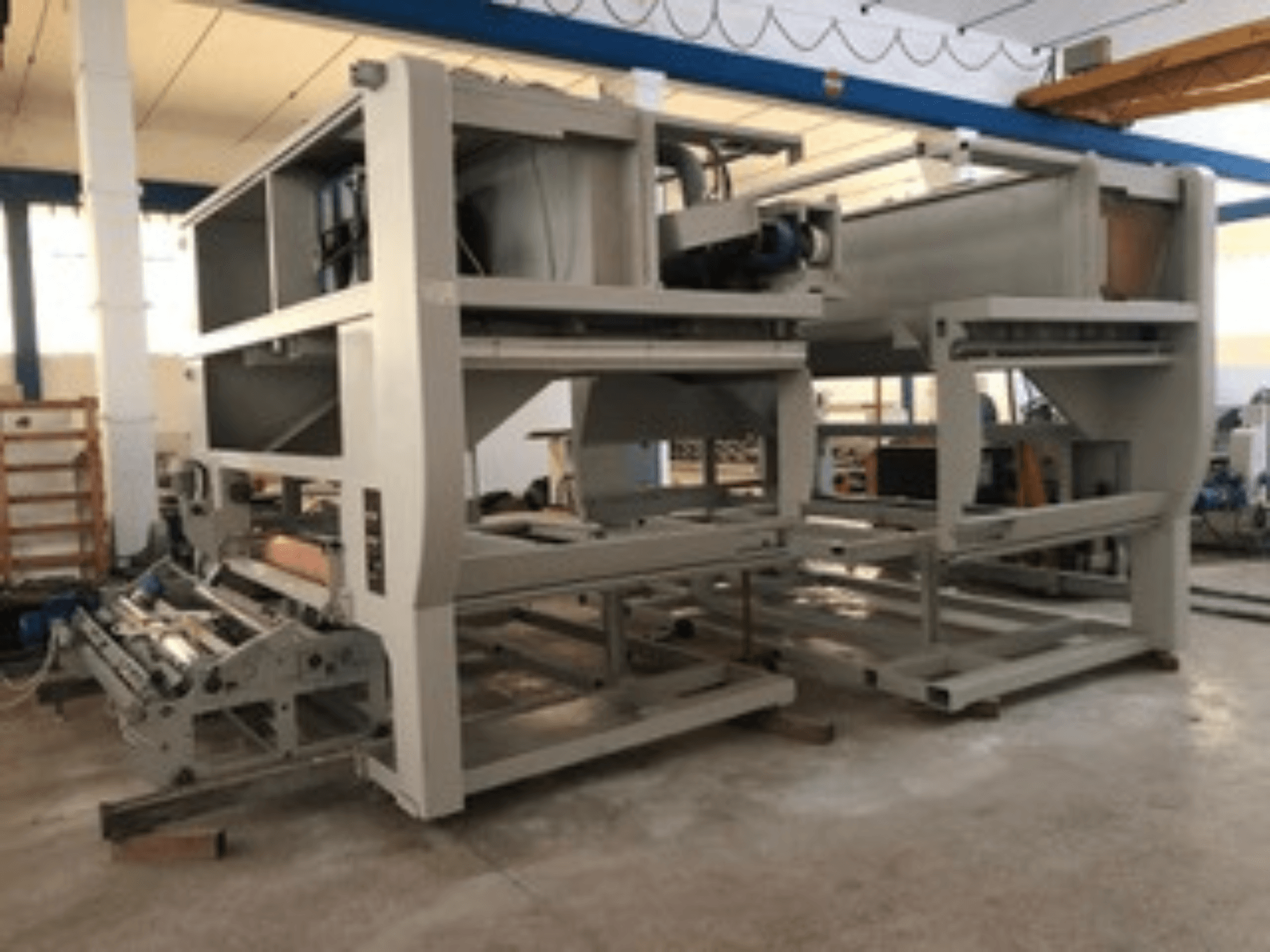 Mitme konveierirulli ja suure konstruktsiooniga tööstuslik masin; külgvaade, hall värv, asub hästi valgustatud tehases.