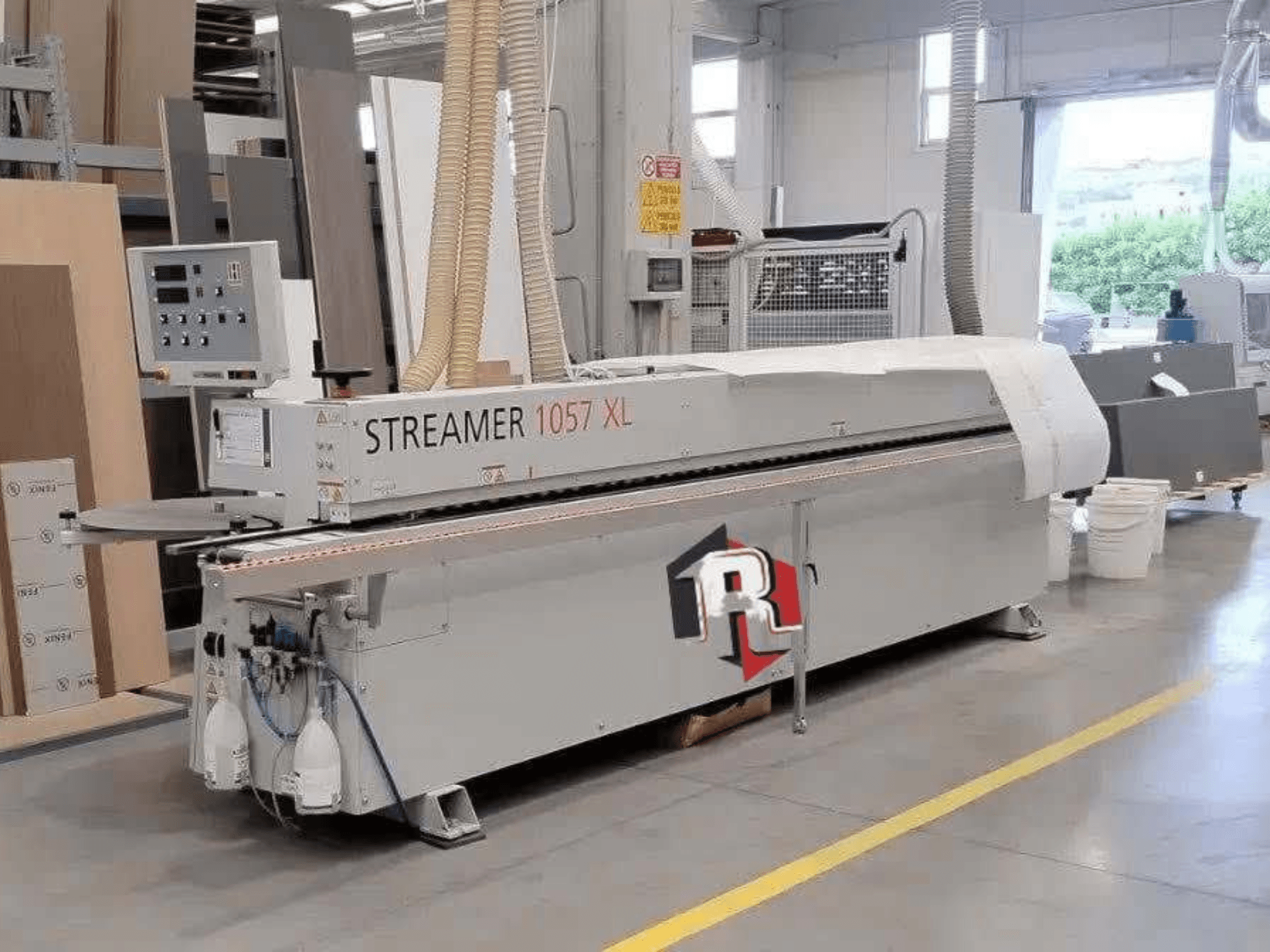 HOLZHER STREAMER 1057 XL servakleebimismasin töökodas, külgvaade, millel on näha juhtpaneel ja õhuvoolikud.