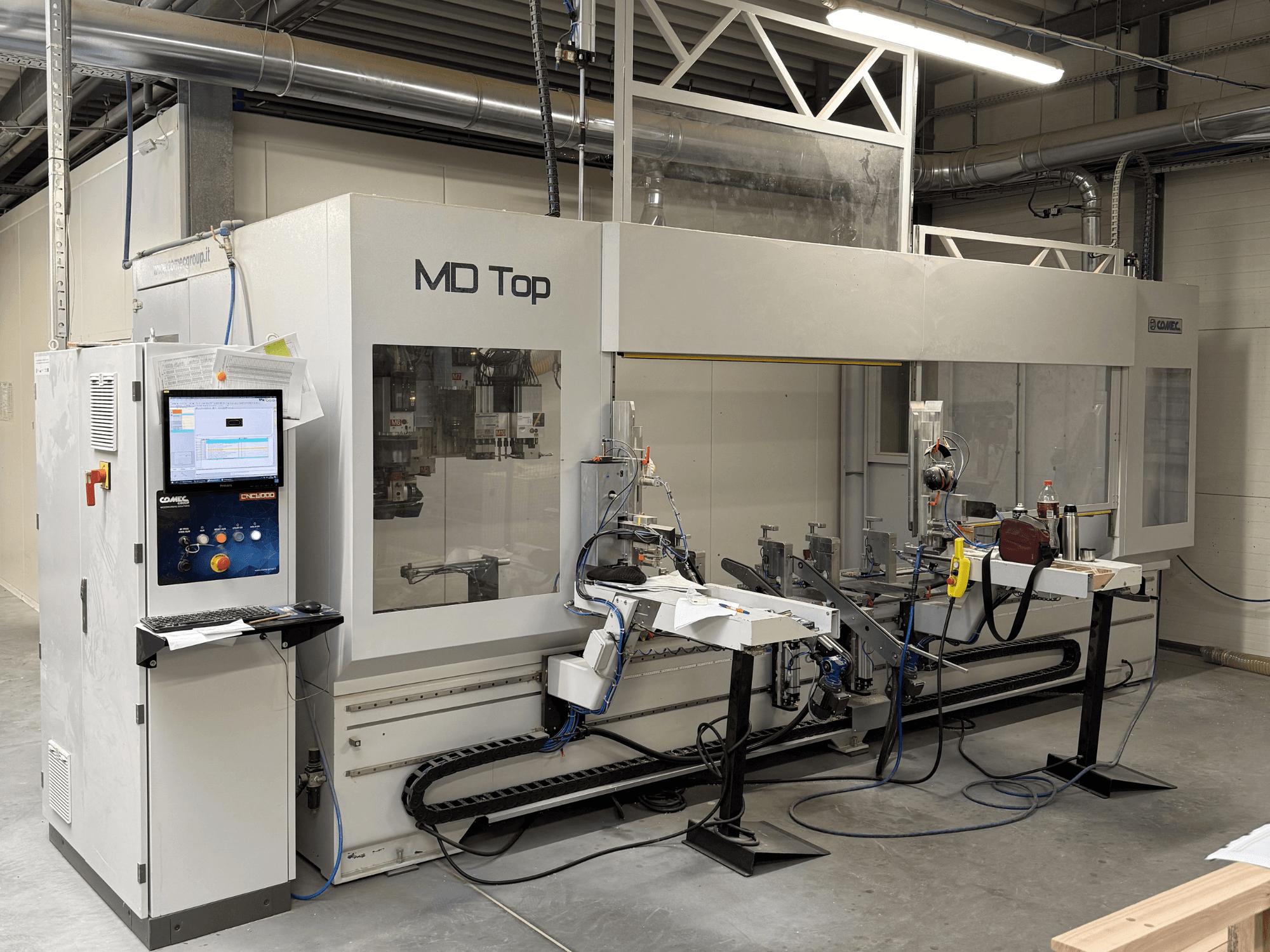 MD Top CNC-tööpink ees, millel on juhtpaneel, robotkäed ning tööruum tööriistade ja materjalidega.