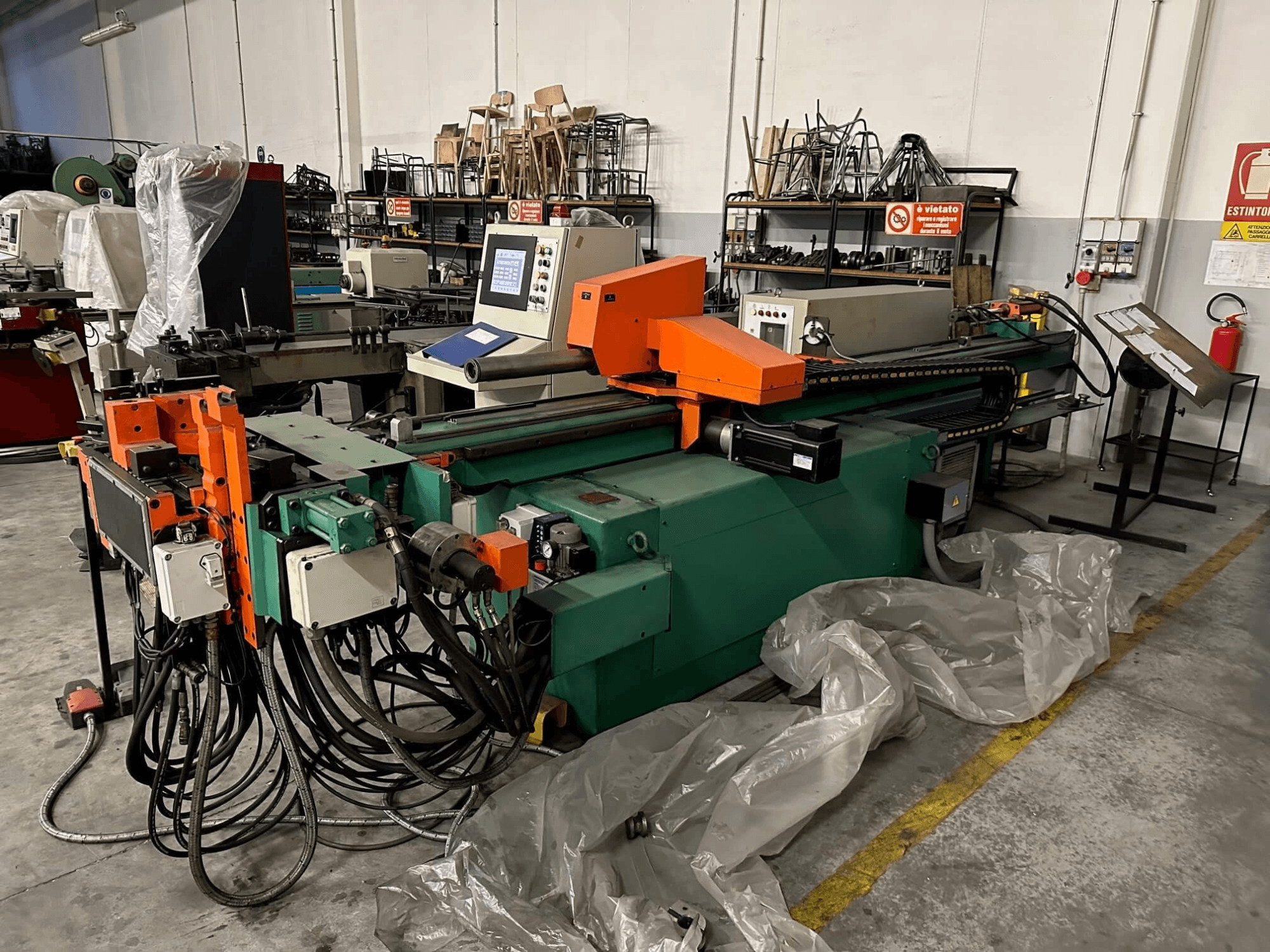 Tööstusmasin oranži ja rohelise korpuse, juhtpaneeli ja arvukate kaablitega, esiplaanilt vaadatuna töökojas.