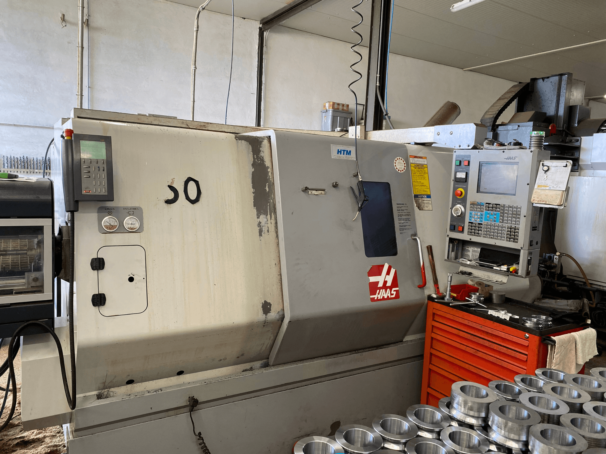 Haasi CNC-pingi juhtpaneel, esivaade, kus on näidatud juhtimisnupud, mõõturid ja läheduses virnastatud metallosad.
