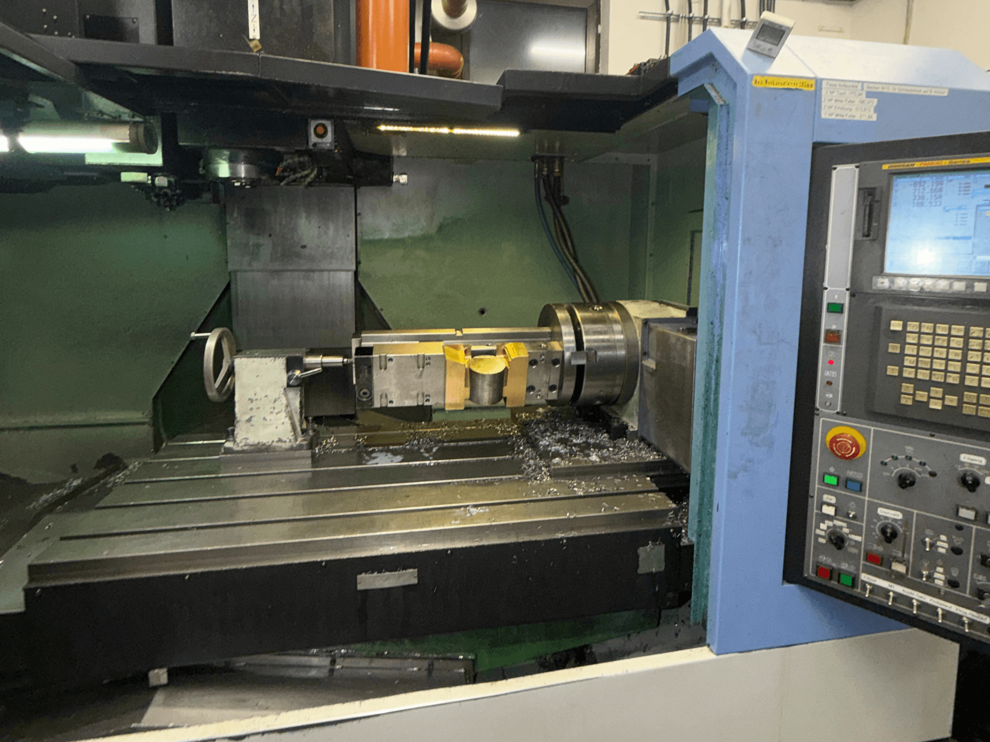 DOOSAN DNM650 vertikaalne töötlemiskeskus, vaade eest, millel on näha lõikeriist ja juhtpaneel ning laual on näha metallilaaste.