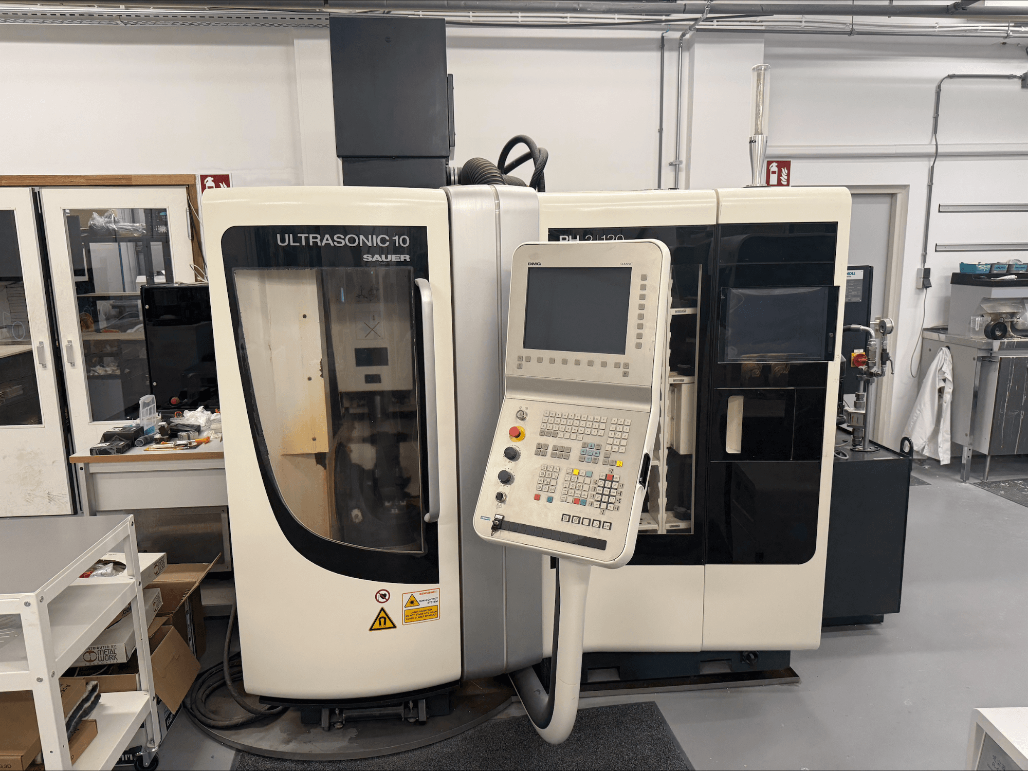 DMG Sauer Ultrasonic 10 + PH 2 | 120 vertikaalne töötlemiskeskus, esiplaanil, juhtpaneel ja suur vaateaken.