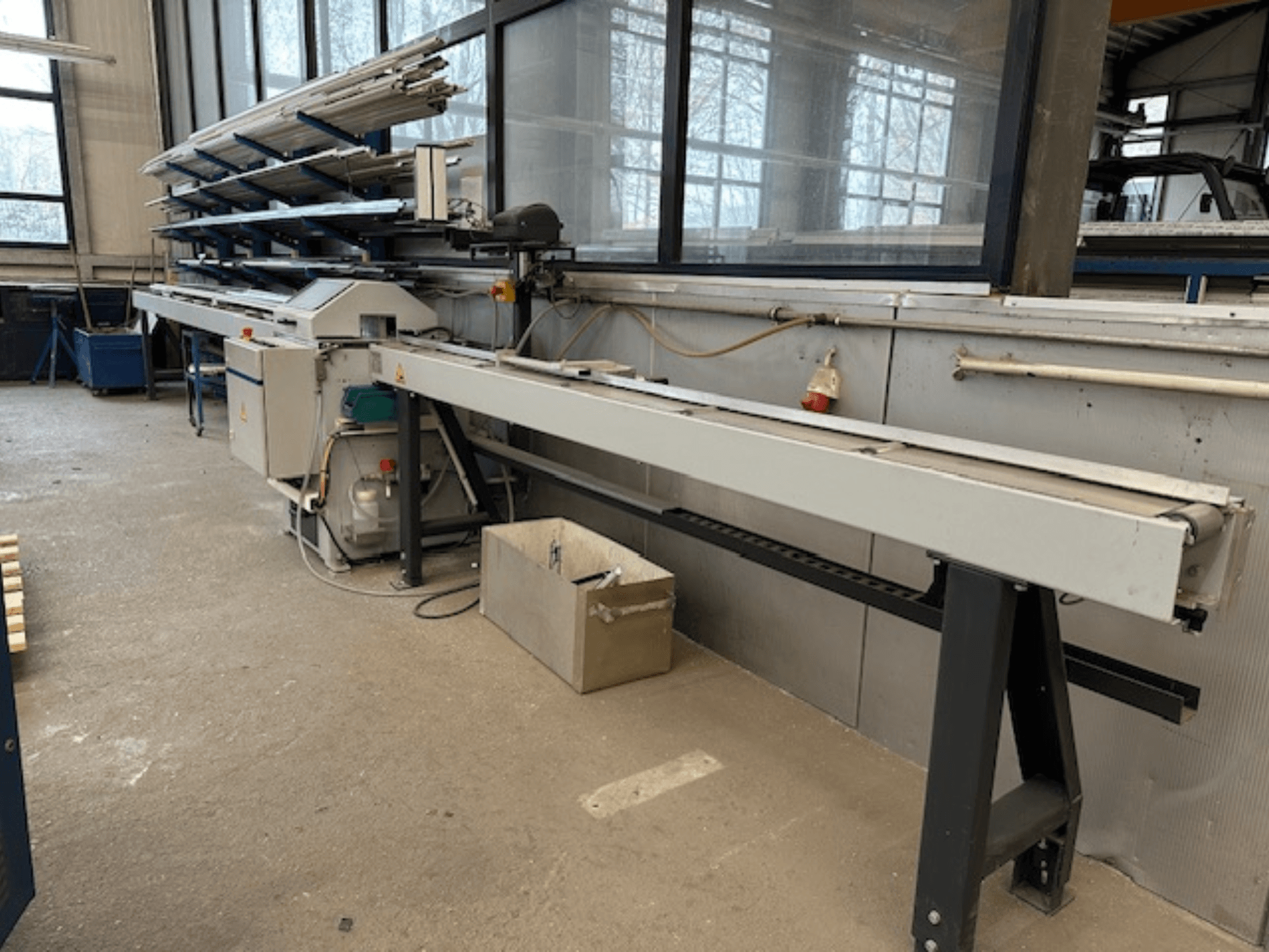 SCHÜCO PGS metallist ketassaag töökojas, külgvaade reguleeritava lõikeplaadiga ja selle kohal oleva metallprofiilide riiuliga.