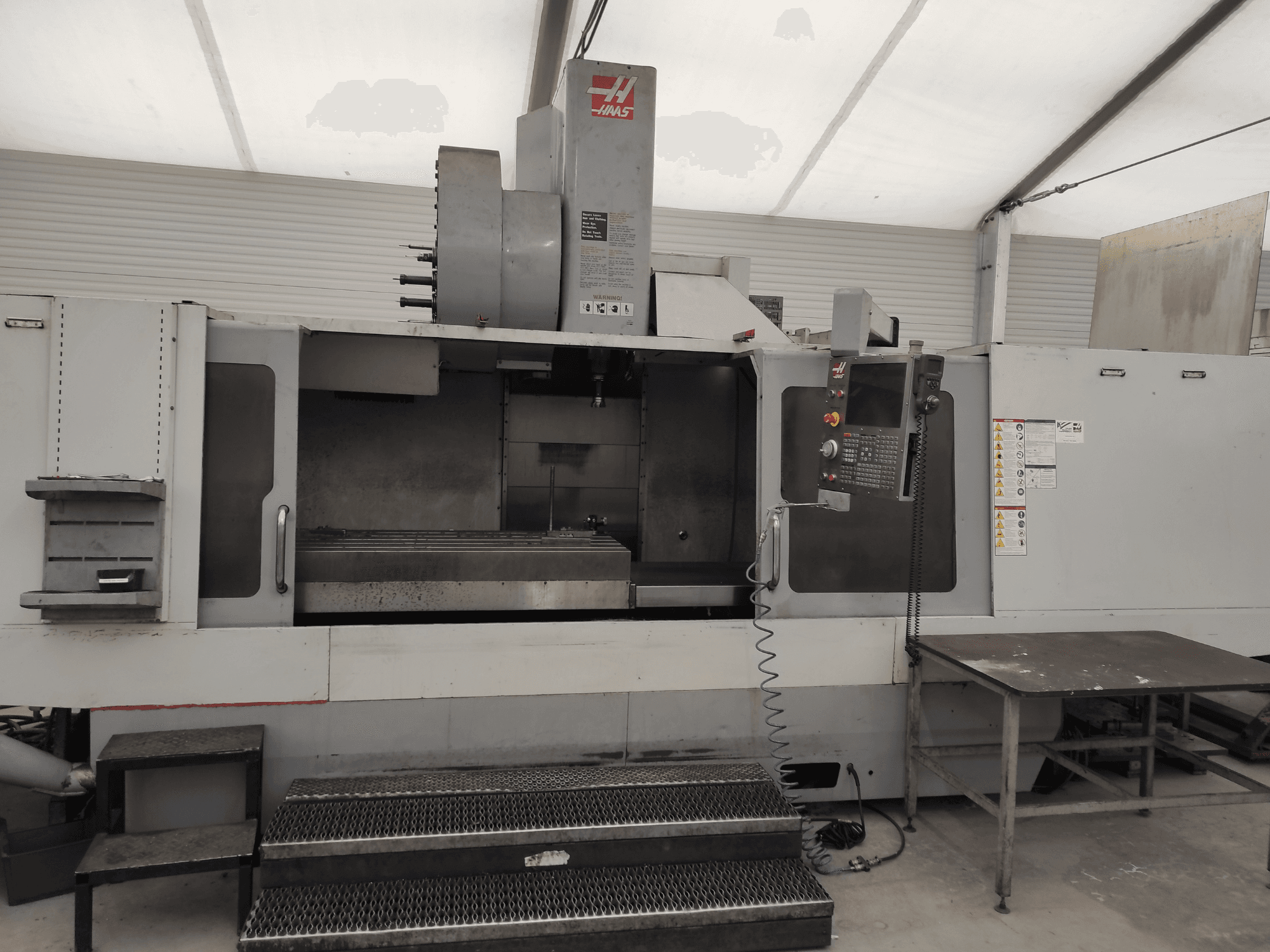 HAAS VF-10/50HE vertikaalne töötluskeskus, esiplaanil on näidatud juhtpaneel, töölaud ja tööks ligipääsetav astmestik.