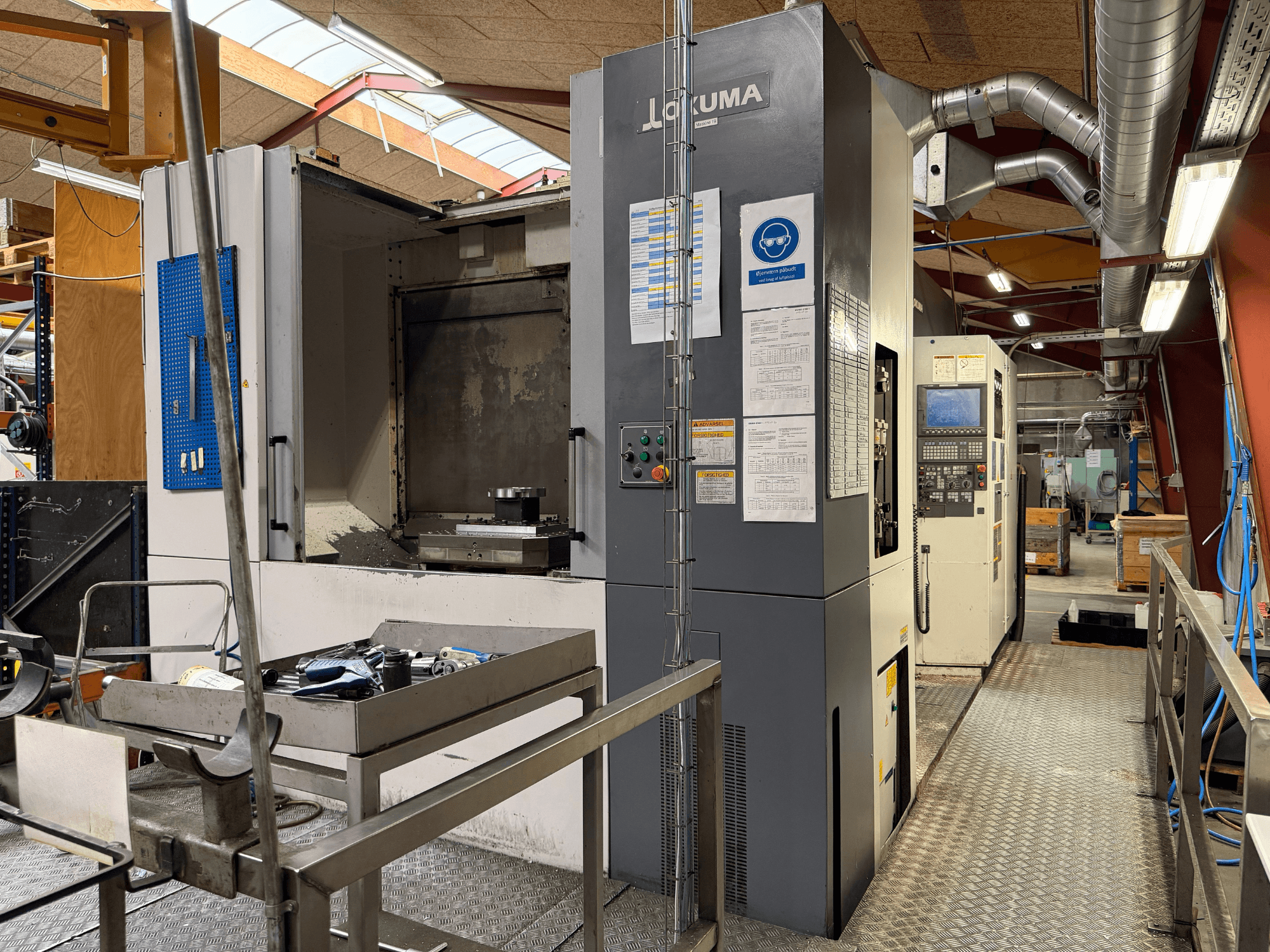 Okuma MA-600HB horisontaalne töötlemiskeskus, vaade eest, millel on näha metalllaual asuvad tööriistad ja masina juhtimispaneel.