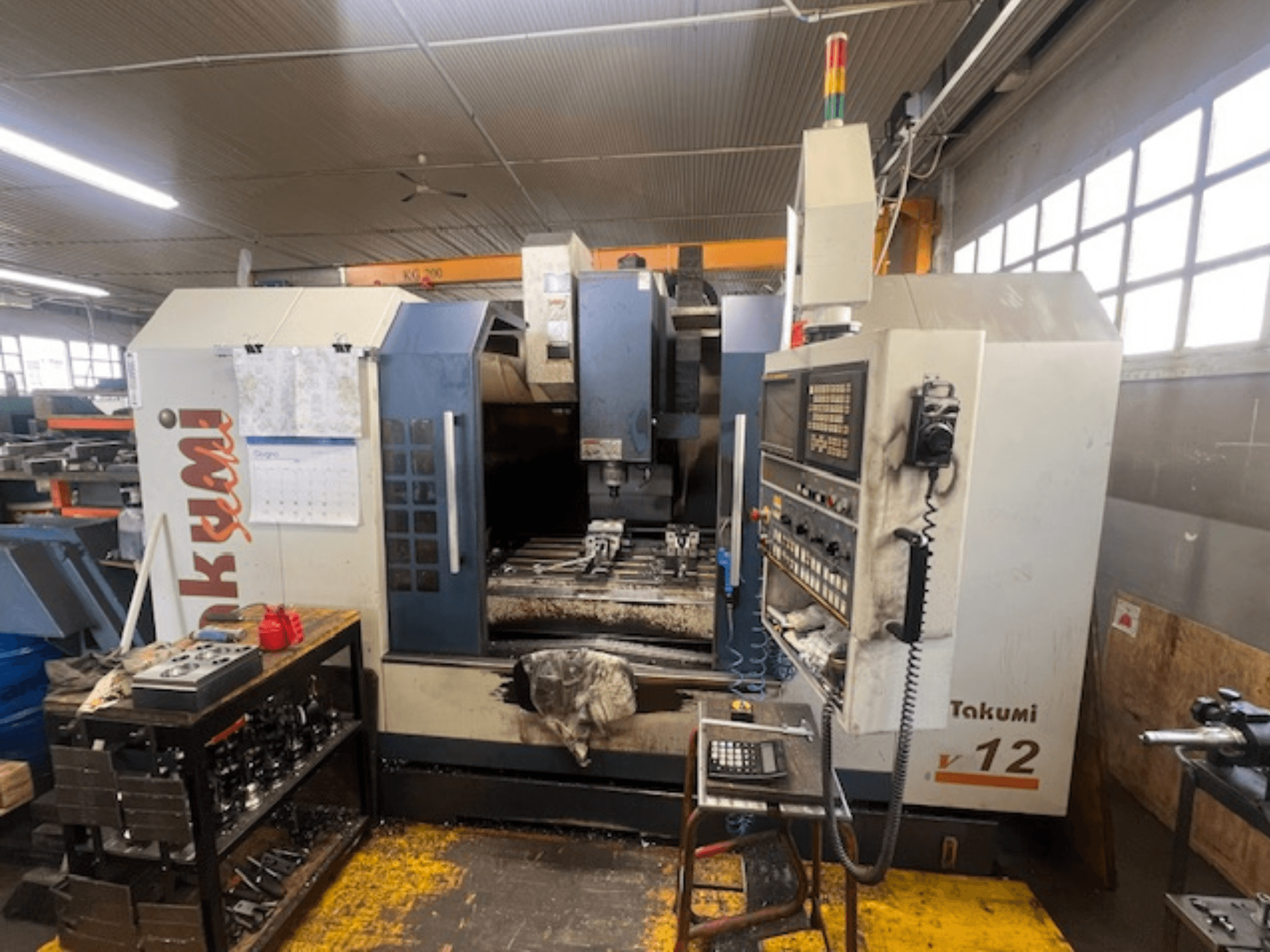 Takumi V12 CNC-freespingi külgvaade, millel on näha juhtpaneel, lõikepind ja tööriistad tööjaamas.