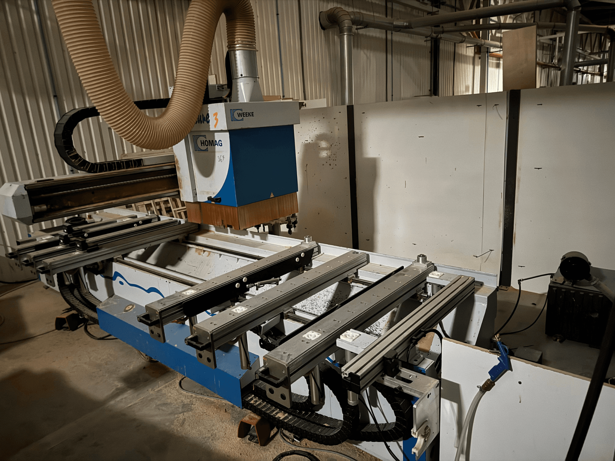 HOMAGi CNC-tööpink sinise ja valge disainiga, külgvaates, millel on liuglevad rööpad, tolmueemaldussüsteem ja paigaldatud tööriistad.