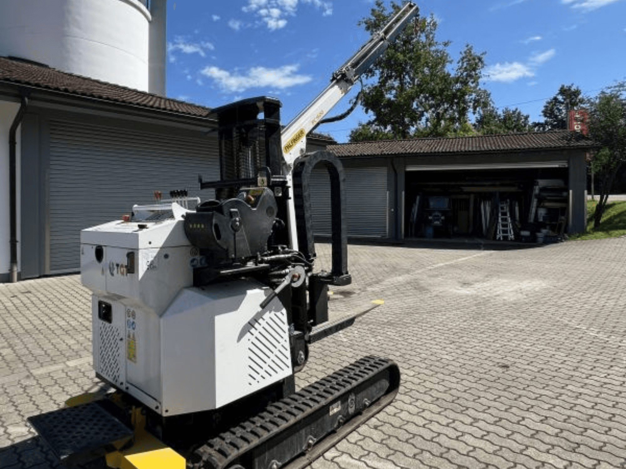 TGI ehitusmiinikraana, külgvaade, kus on näha rööpad ja paigaldatud poom, pargitud garaaži juures telliskivipinnal.