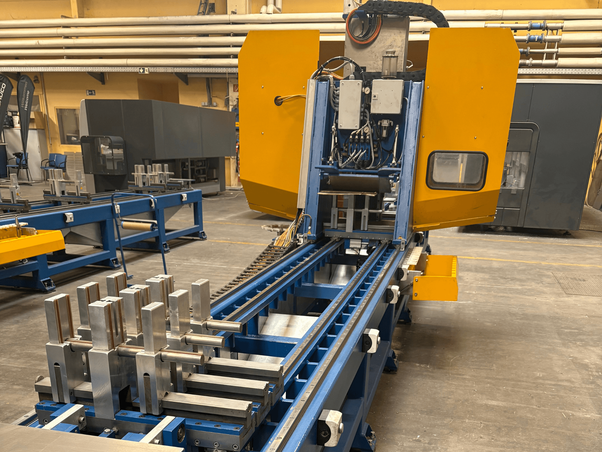 SCHÜCO PBX AL universaaltöötluskeskuse esiplaanil, kus näidatakse metallitoorikuid sinisel töötlemisplatvormil.