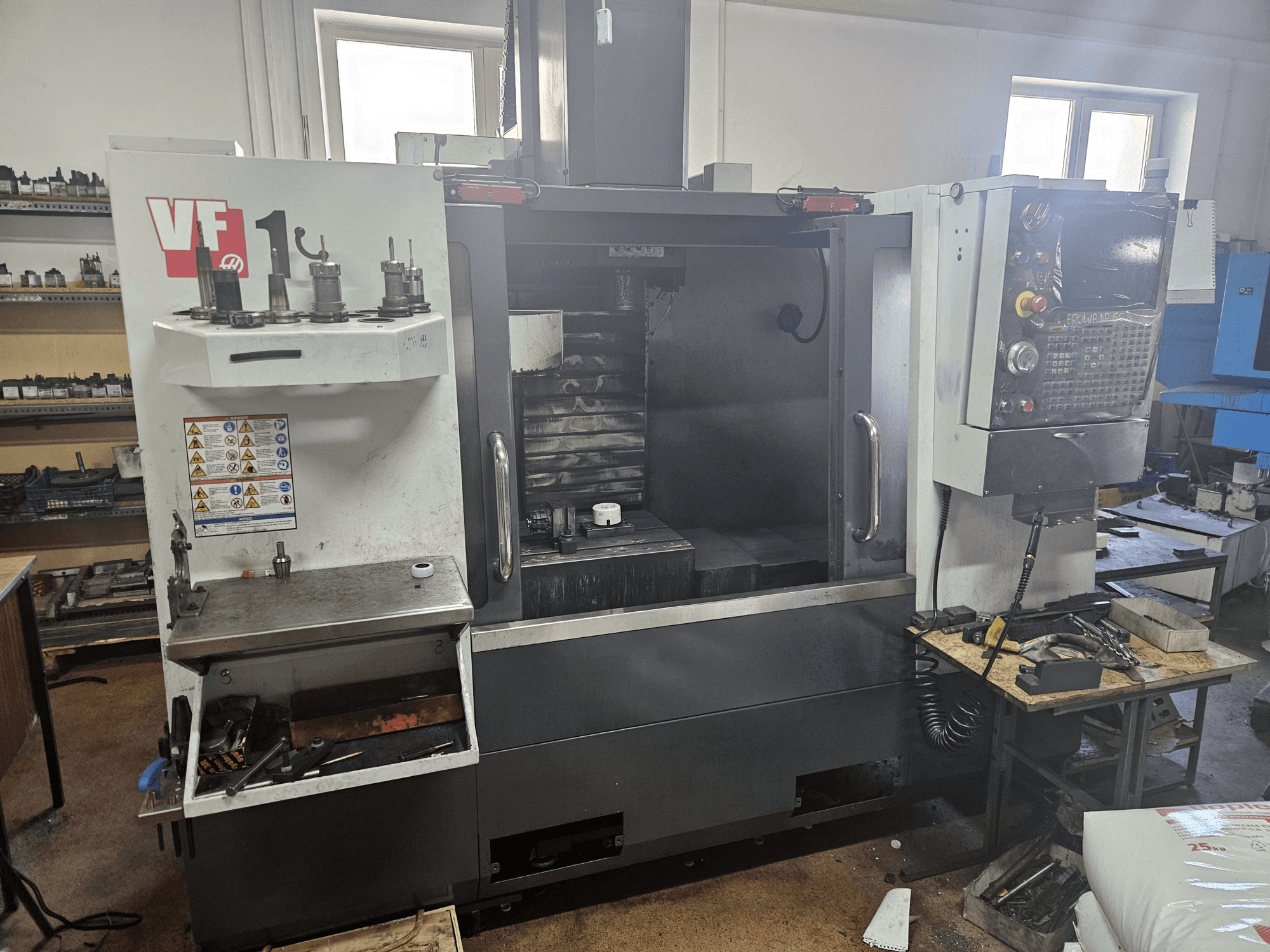 HAAS VF-1 vertikaalne töötlemiskeskus, esiplaanil, tööriistad küljel, juhtpaneel nähtav ja tööruum taustal.