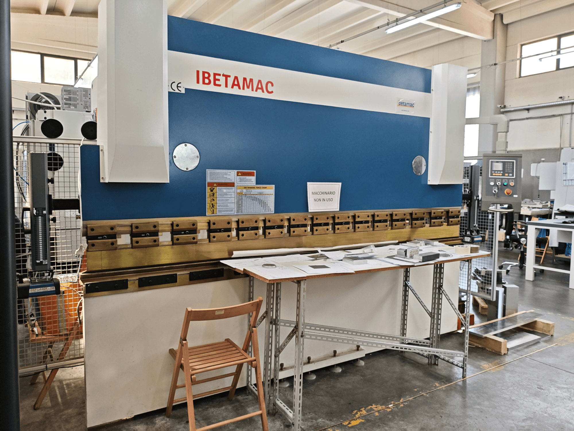 Töökojas asuv IBETAMAC 3200 100T kantpress, külgvaade, millel on näha juhtpaneel, tööala ja ohutusjuhised.