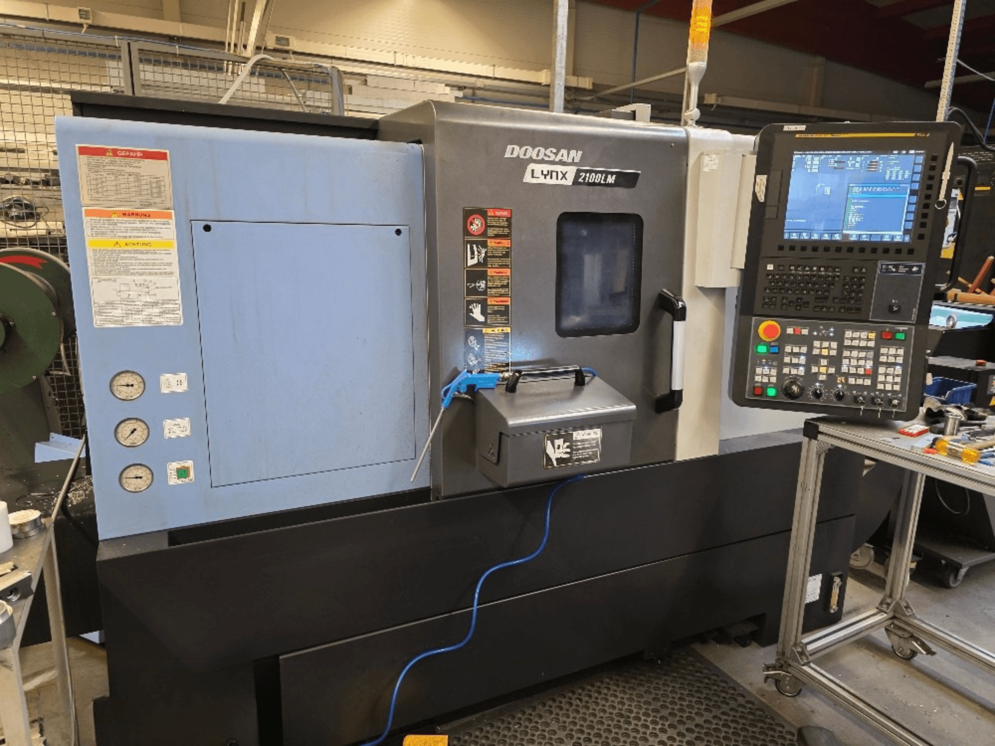Doosan Lynx 2100LM CNC-tööpink, esiplaan, juhtpaneel, rõhumõõturid ja ohutushoiatused.