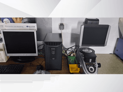 Kaks arvutimonitori, üks Acer ja üks Keyence, musta seadme ja mikroskoobi kõrval, esiplaanilt vaadatuna.
