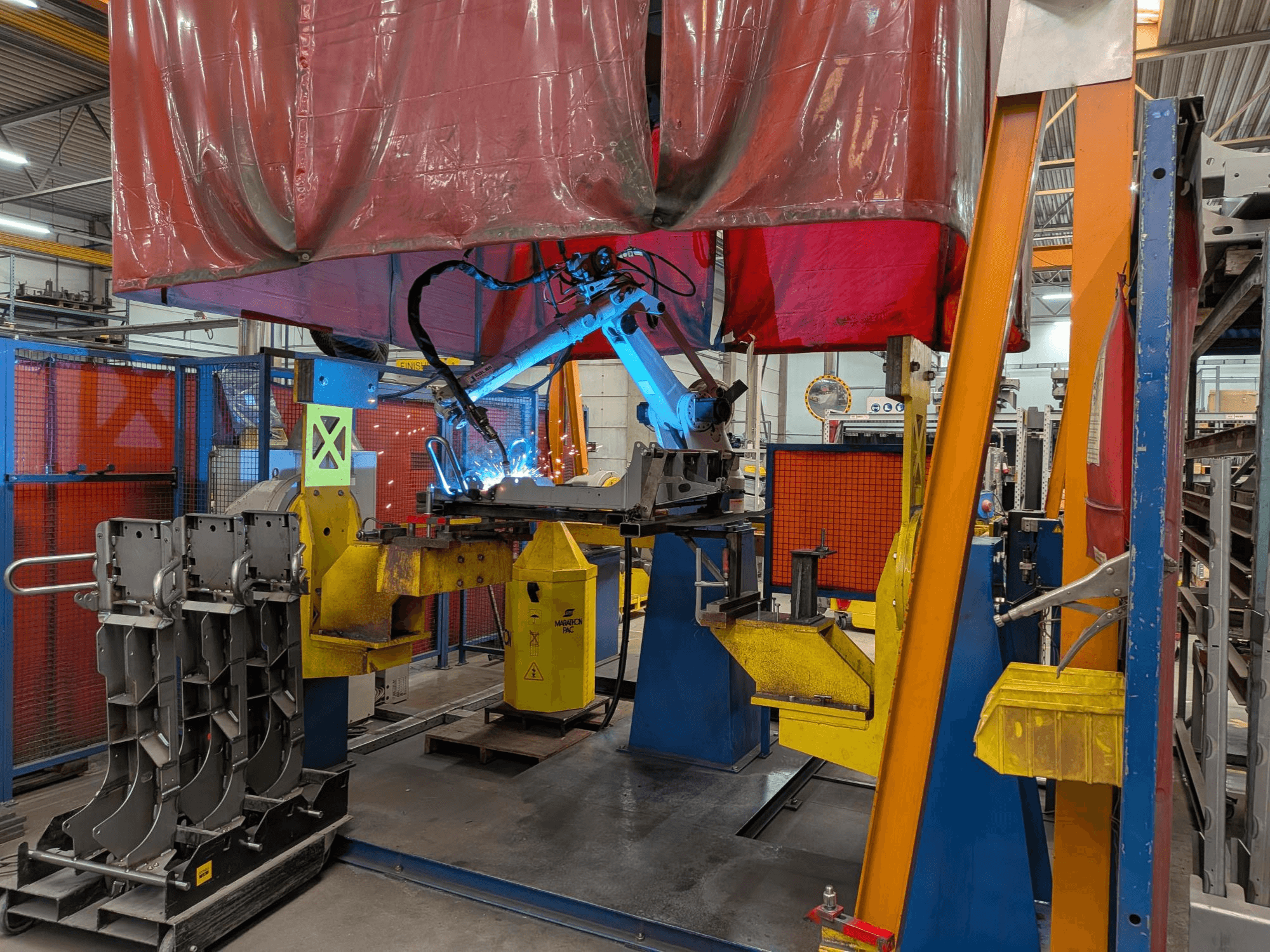 Keevitusrobot OTC Daihen DR4200 töös, vaadatuna eestpoolt, koos helesinise keevituskaare ja kaitsekilbiga.