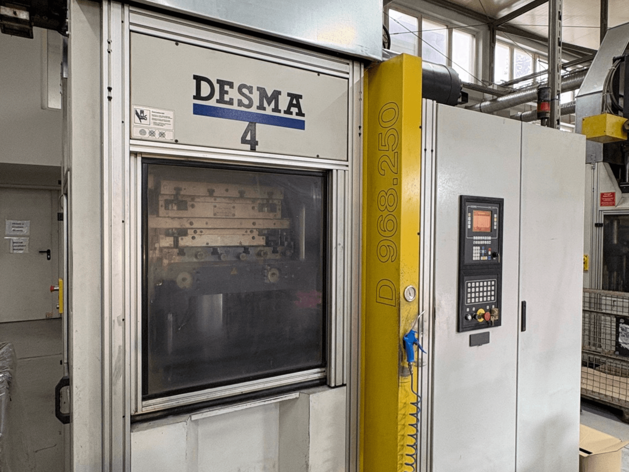 Vertikaalne survevalu masin Kloeckner Desma 968.250, esiplaanil on näidatud juhtpaneel ja masina üksikasjad.