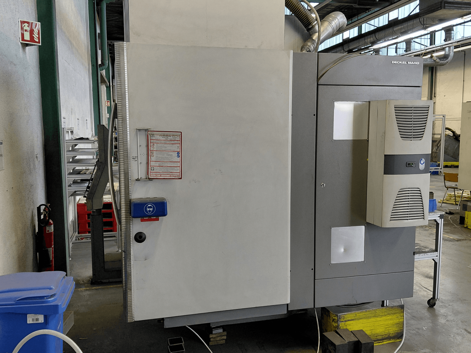 DECKEL MAHO DMC 635 V vertikaaltöötluskeskuse külgvaade koos juhtpaneeli ja ohutussiltidega.