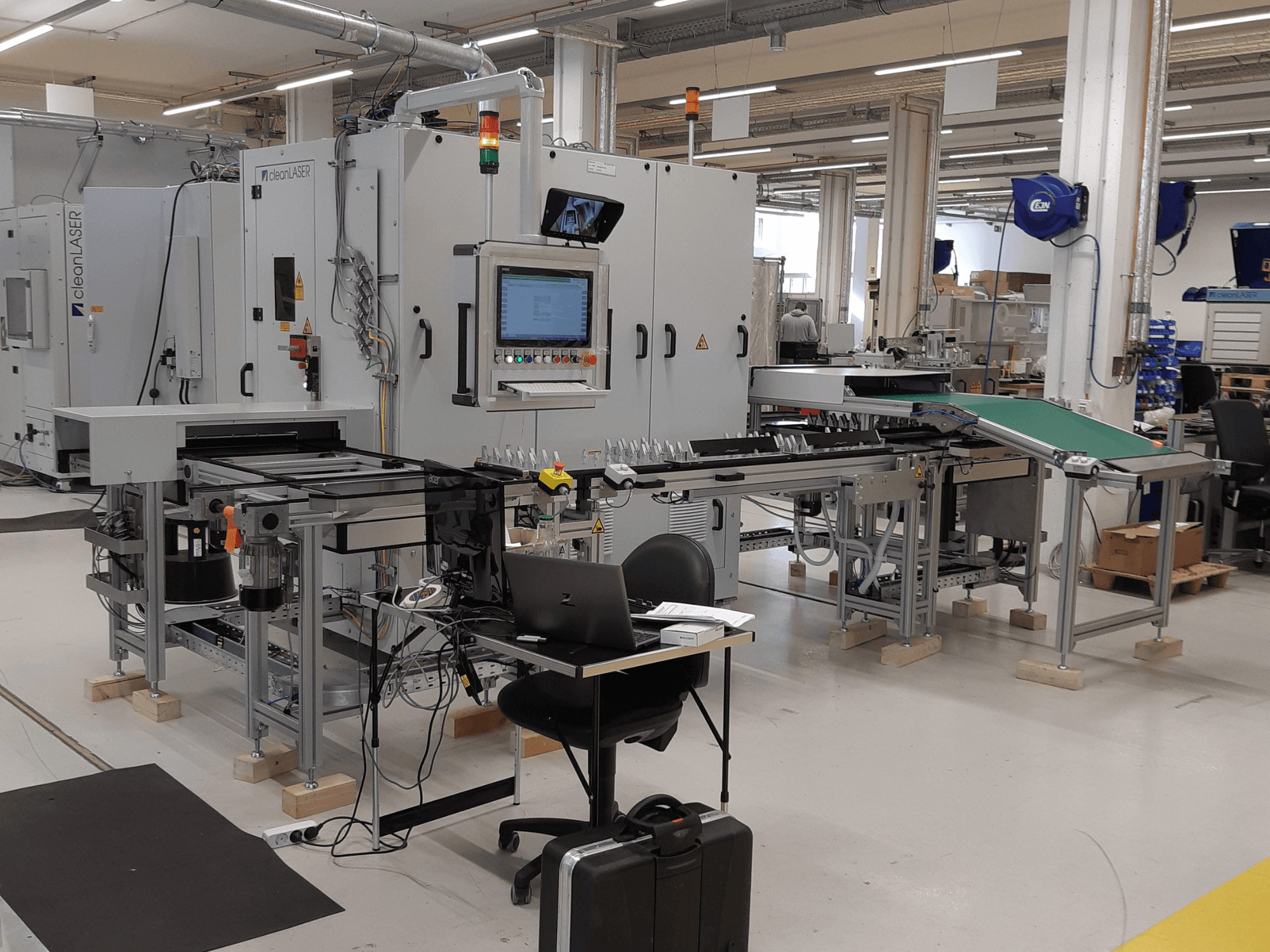 CLEAN LASER clean CELL 3220 CL600 tööpink, vaade eest, kus on näha juhtpaneel, konveier ja töötsoon töökoha keskkonnas.
