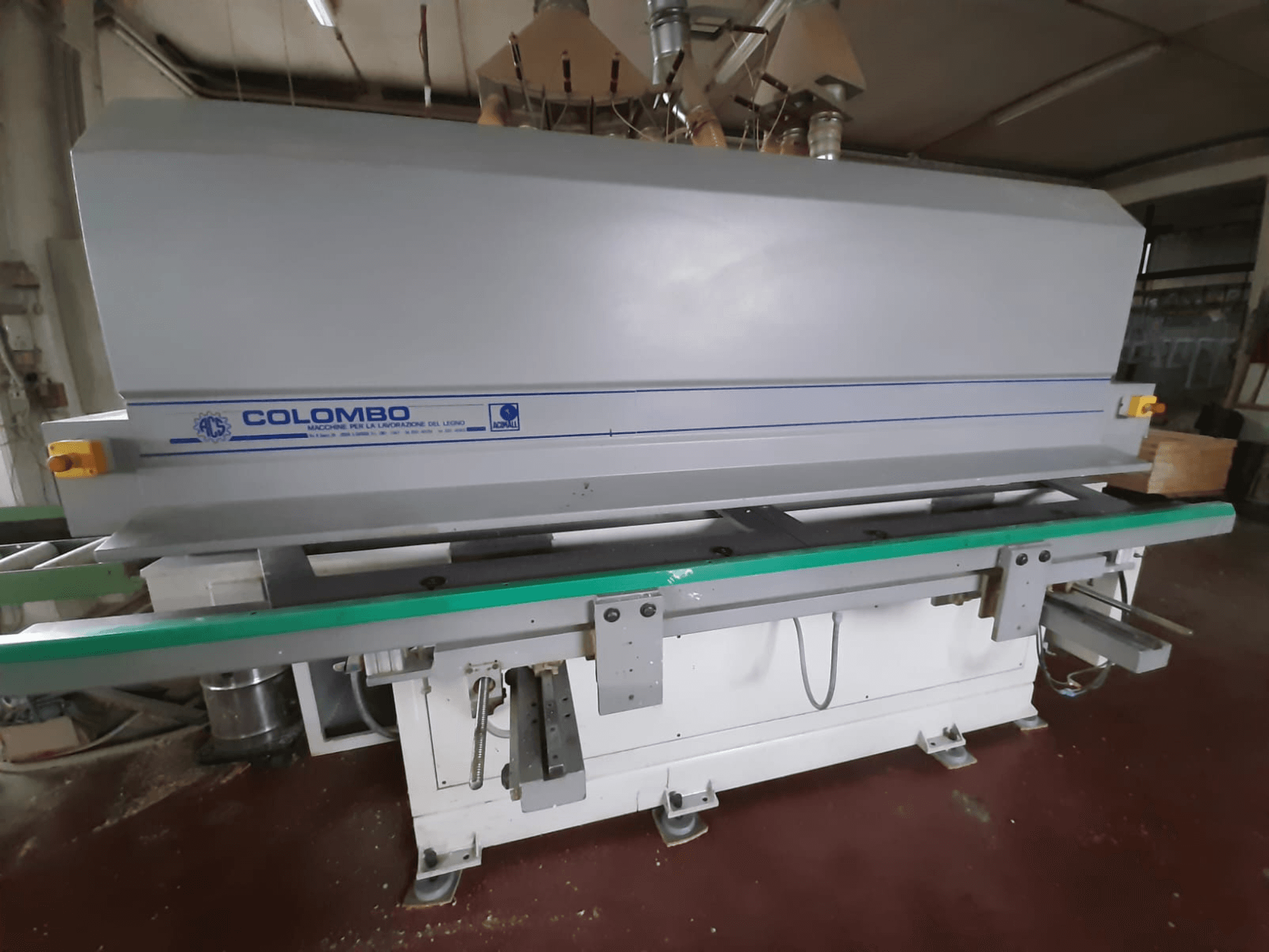 Colombo puidutöötlemismasin, esiplaanil, millel on pikk roheline laud, juhtnupud ja siniste aktsentidega hall korpus.
