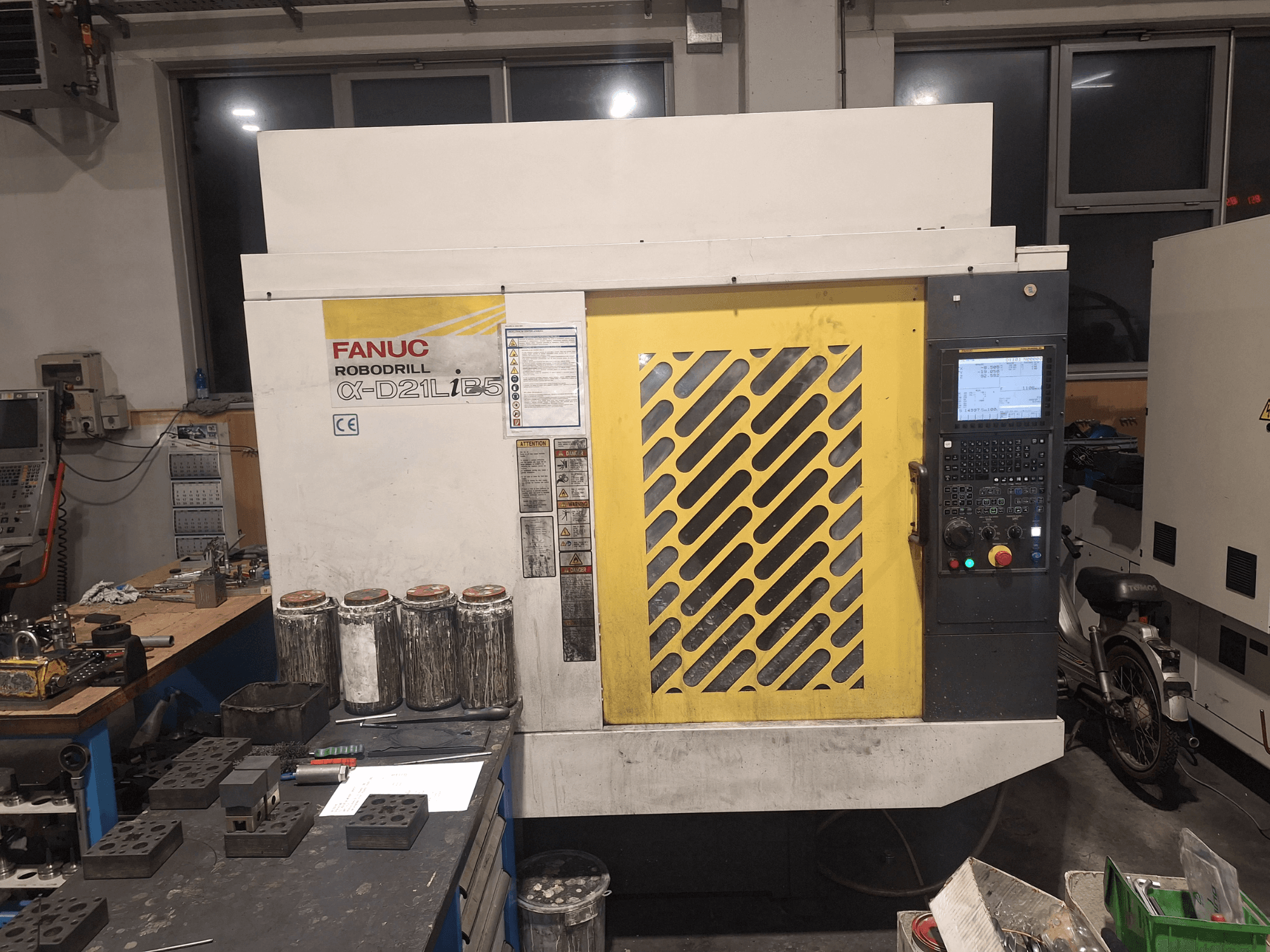 FANUC Robodrill α-D21LiB5 esivaade, millel on näidatud juhtpaneel, kollane võre ja lähedalasuvad tööriistad tööpinkidel.