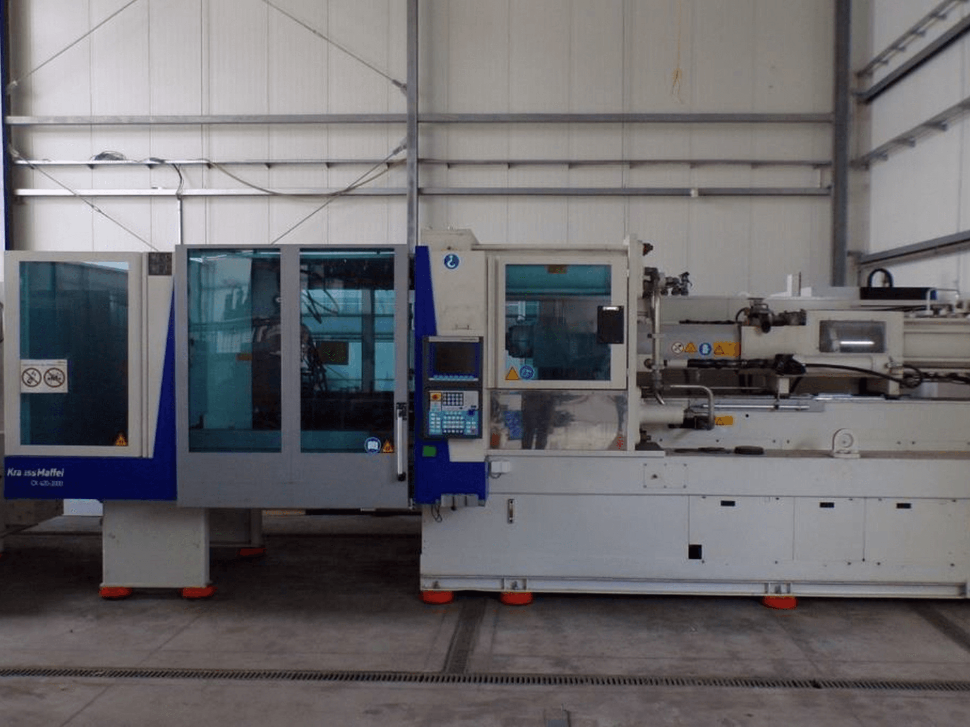 KraussMaffei survevalu masin, külgvaade, millel on juhtpaneel ja ohutusnäidikud, nähtavad tehases.