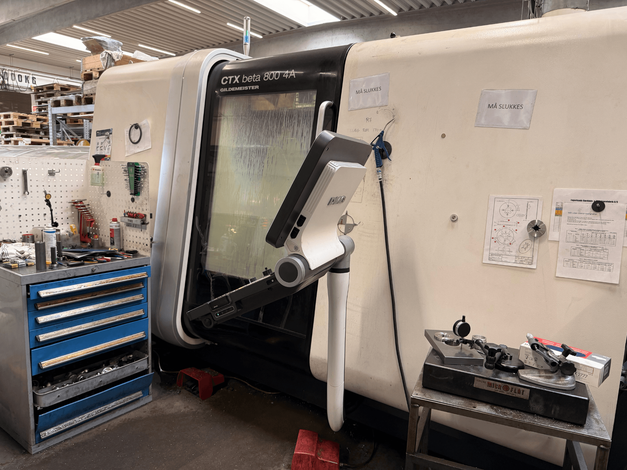 DMG MORI CTX Beta 800 4a vertikaalne treipingi töökojas, mille lähedal on juhtvarras ja tehnilised dokumendid.