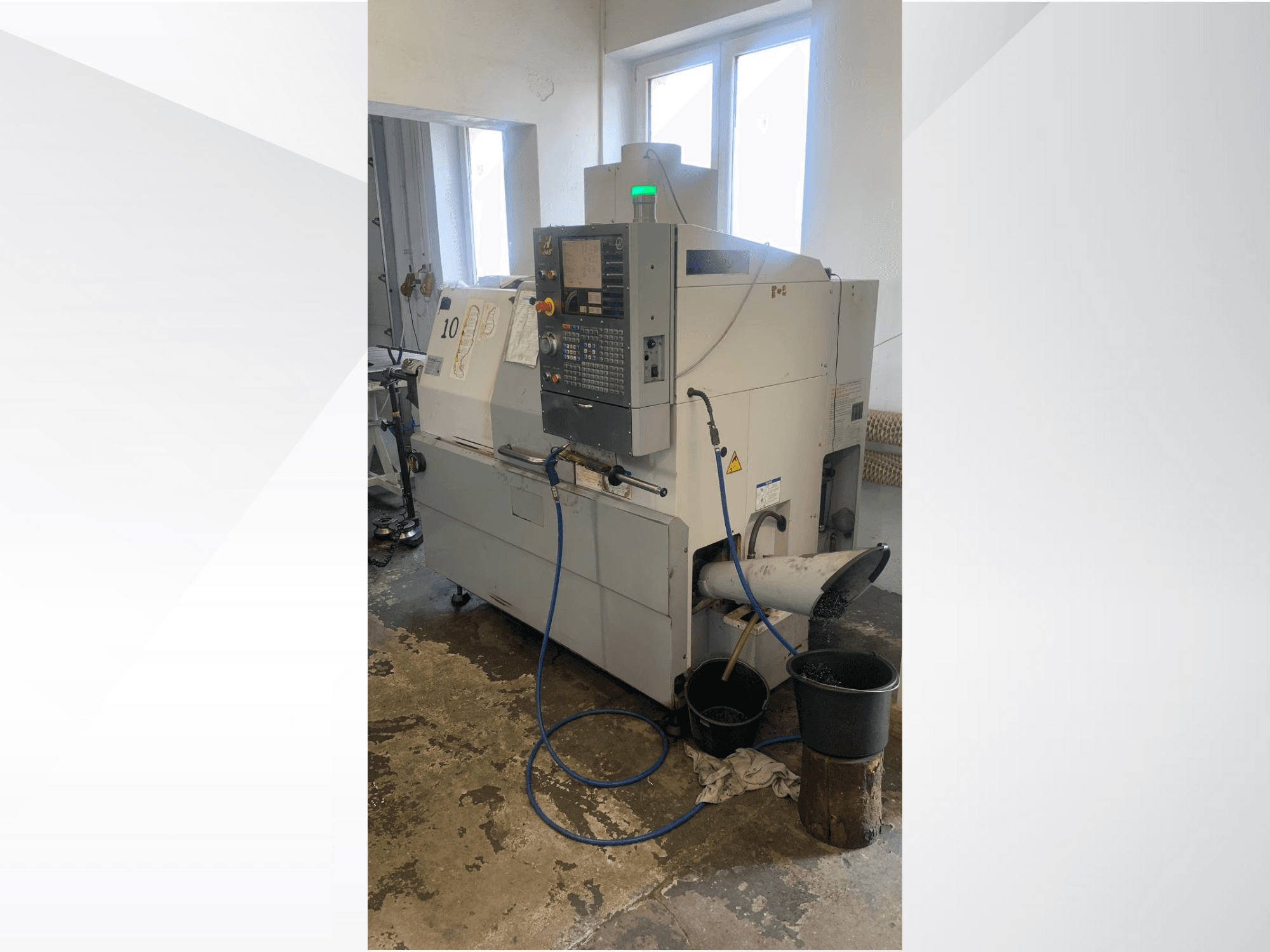 Haasi CNC-pingi mudel koos juhtpaneeliga, külgvaates, millel on jahutusvedeliku liin, jäätmekanal ja allpool olevad hoiukonteinerid.