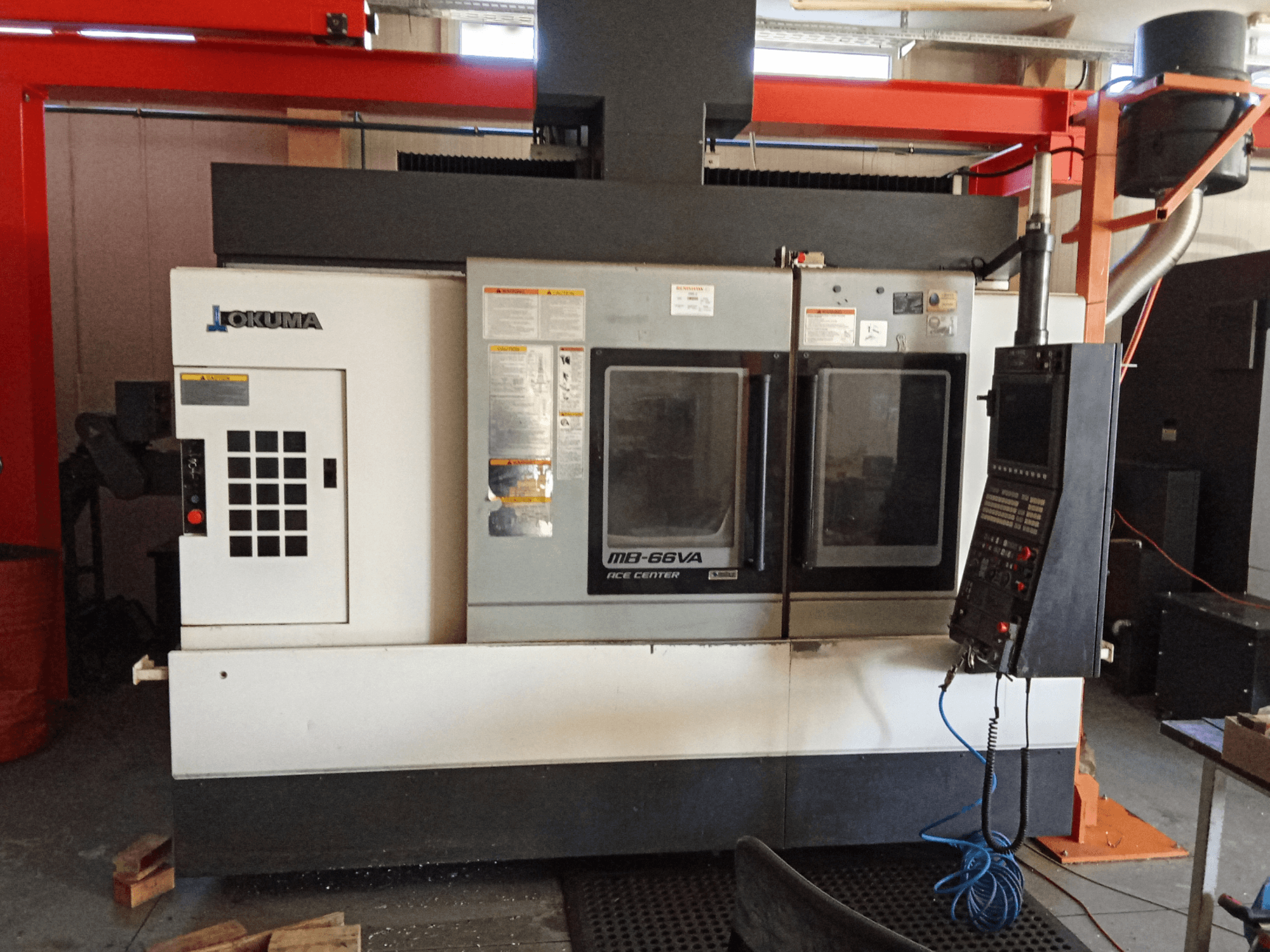 Okuma MB-66VA vertikaalne töötluskeskus, esiplaanil on juhtpaneel ja kaks vaateakent tööriistadele juurdepääsuks.