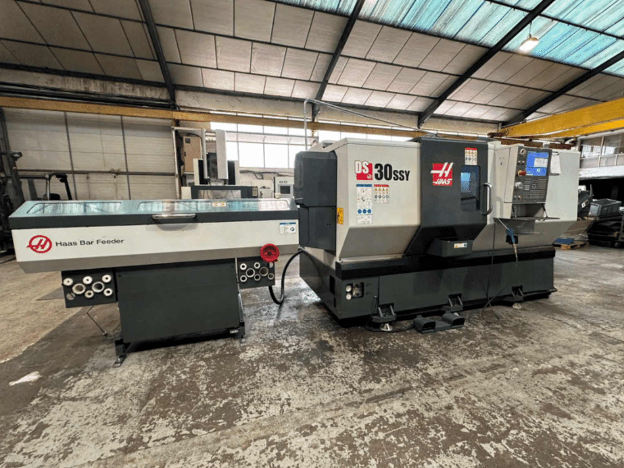 Haas DS-30SSY CNC-teeninduspingi ja Haasi vardasööturiga, külgvaade, kus on näidatud juhtpaneel ja etteandemehhanism töökojas.