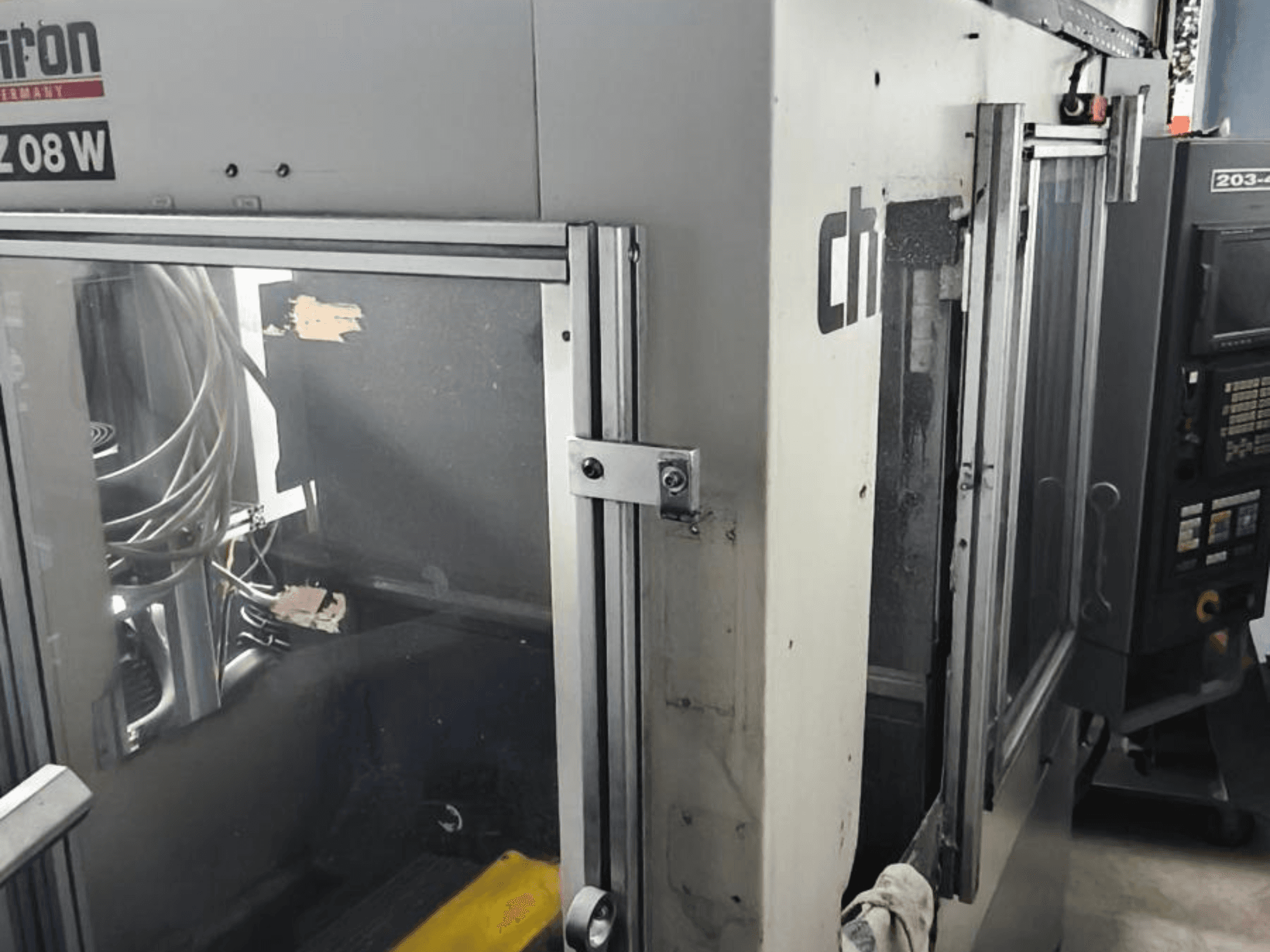 Vertikaalne töötluskeskus CHIRON FZ 08 W, esiplaanil on juhtpaneel ja osaliselt avatud uksed koos nähtavate sisemiste komponentidega.