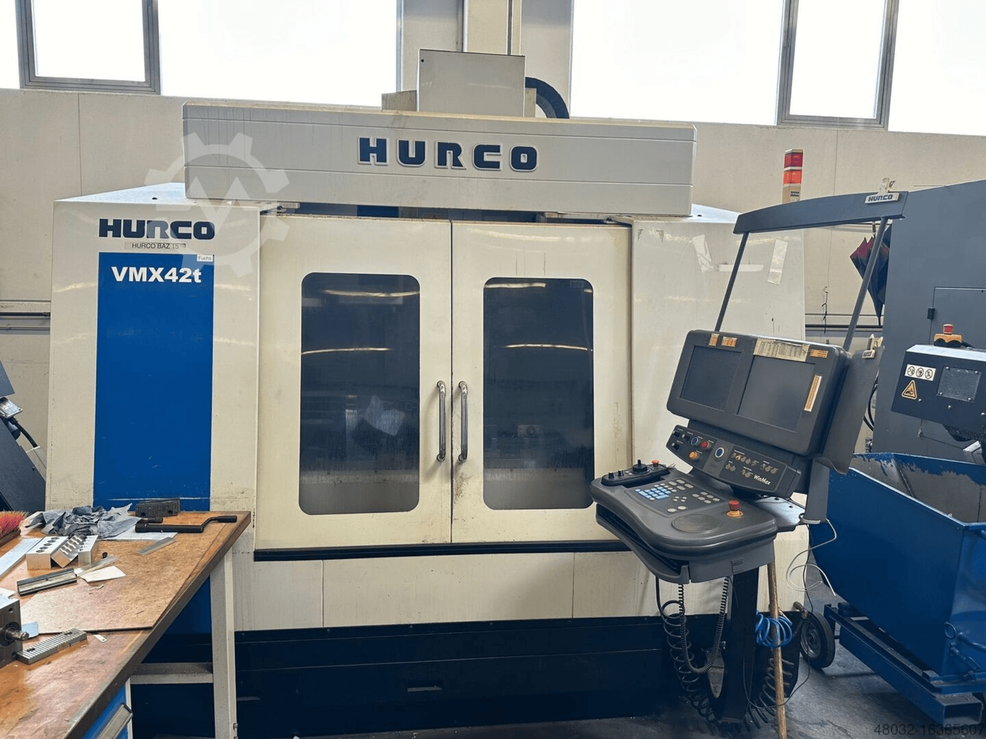 Hurco VMX42t vertikaalne töötlemiskeskus, vaade eest, millel on näha juhtpaneel ja töötlemiskeskuse sisemus koos tööriistade ja töödeldavate detailidega.