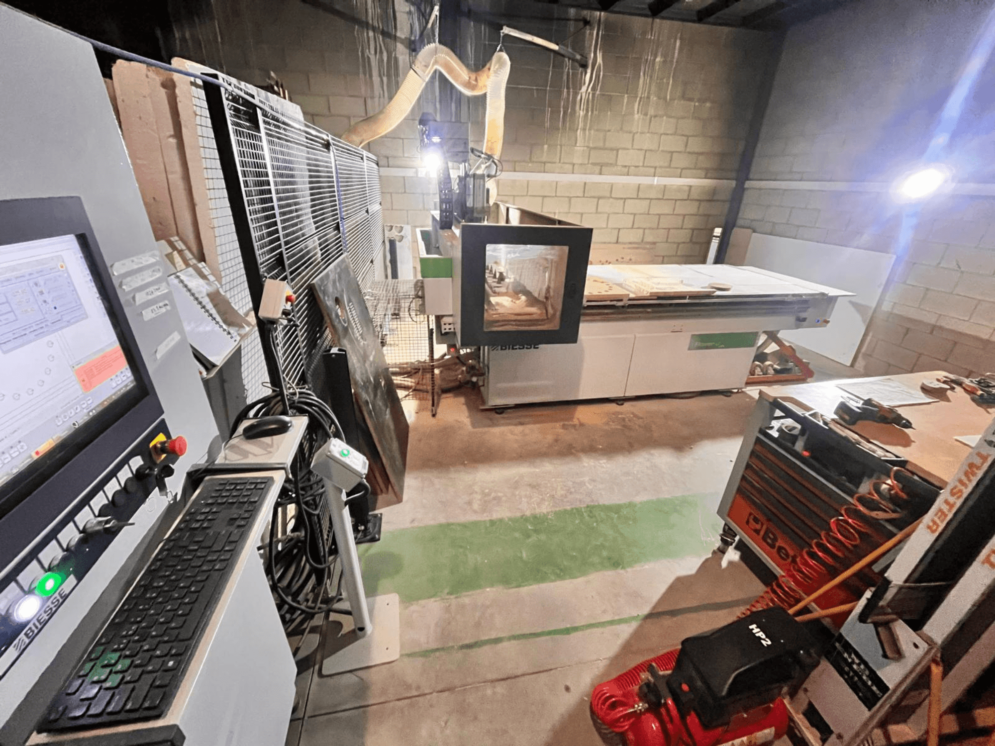 Biesse CNC-tööpink töökojas, külgvaates on näha juhtpaneel, tolmueemaldus, tööriistad ja erinevad materjalid laual.