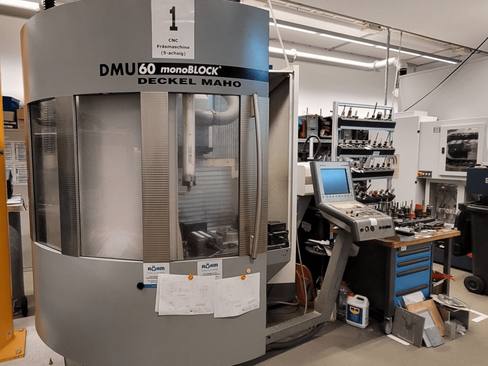 CNC-freesping DECKEL MAHO DMU 60 monoBLOCK esiplaanil, mille kõrval on juhtpaneel ja tööriistade hoidla.