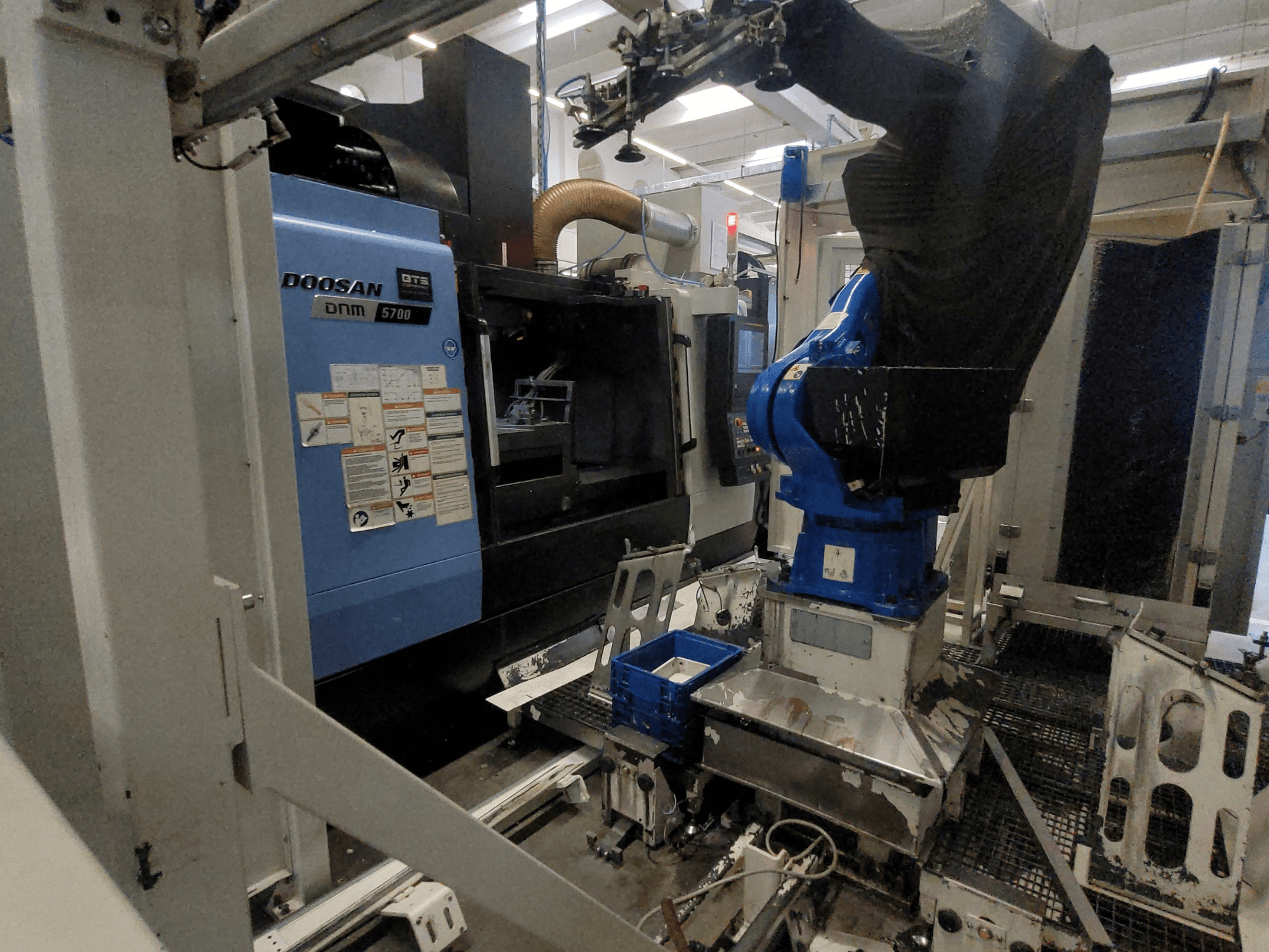 DOOSAN DNM 5700 vertikaalne töötlemiskeskus tehase keskkonnas, millel on näha selle esivaade ja robotkäe integreerimine.