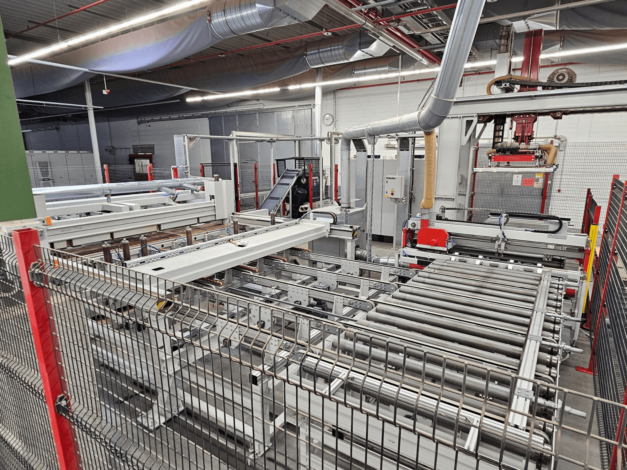 HOLZMA HPP81-3200 tahvlisaag esiplaanil, millel on konveierirullid ja masinaosad töökojas.