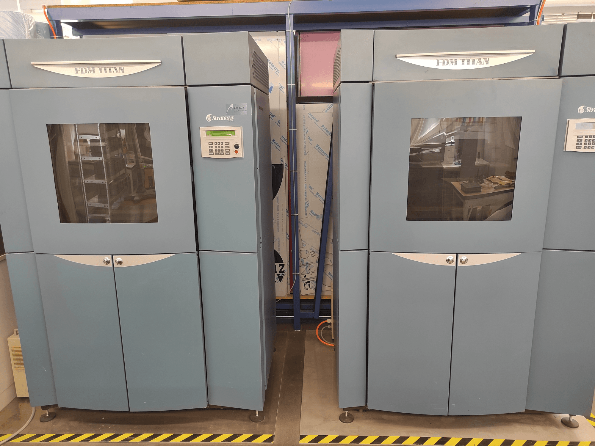 Stratasysi FDM TitanTI 3D-printer, vaade eest, millel on kaks ust ja juhtpaneel, paigutatud tööstuslikku keskkonda.